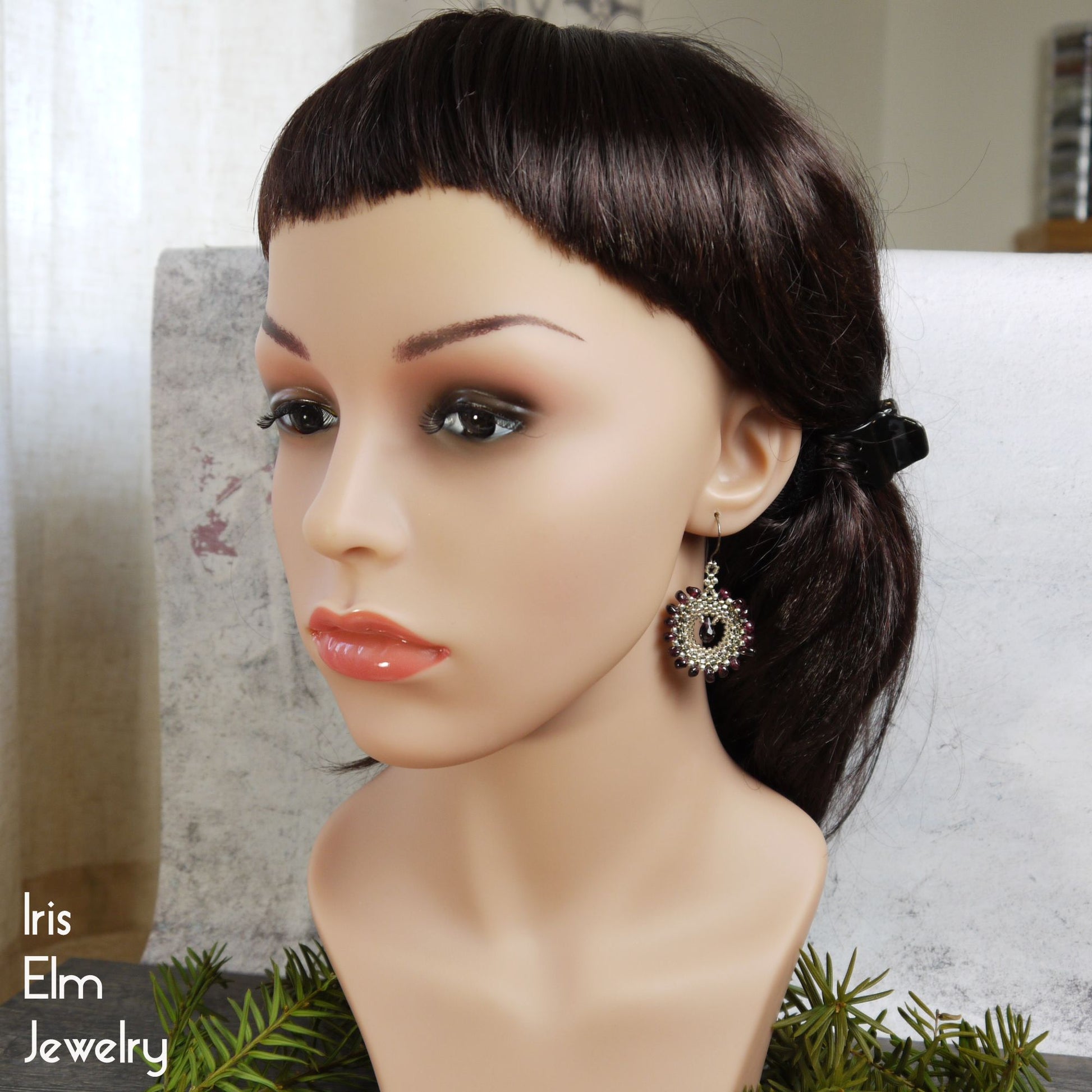 Mannequin head with dark hair and bohemian garnet earrings on a neutral background, featuring 'Iris Elm Jewelry'.