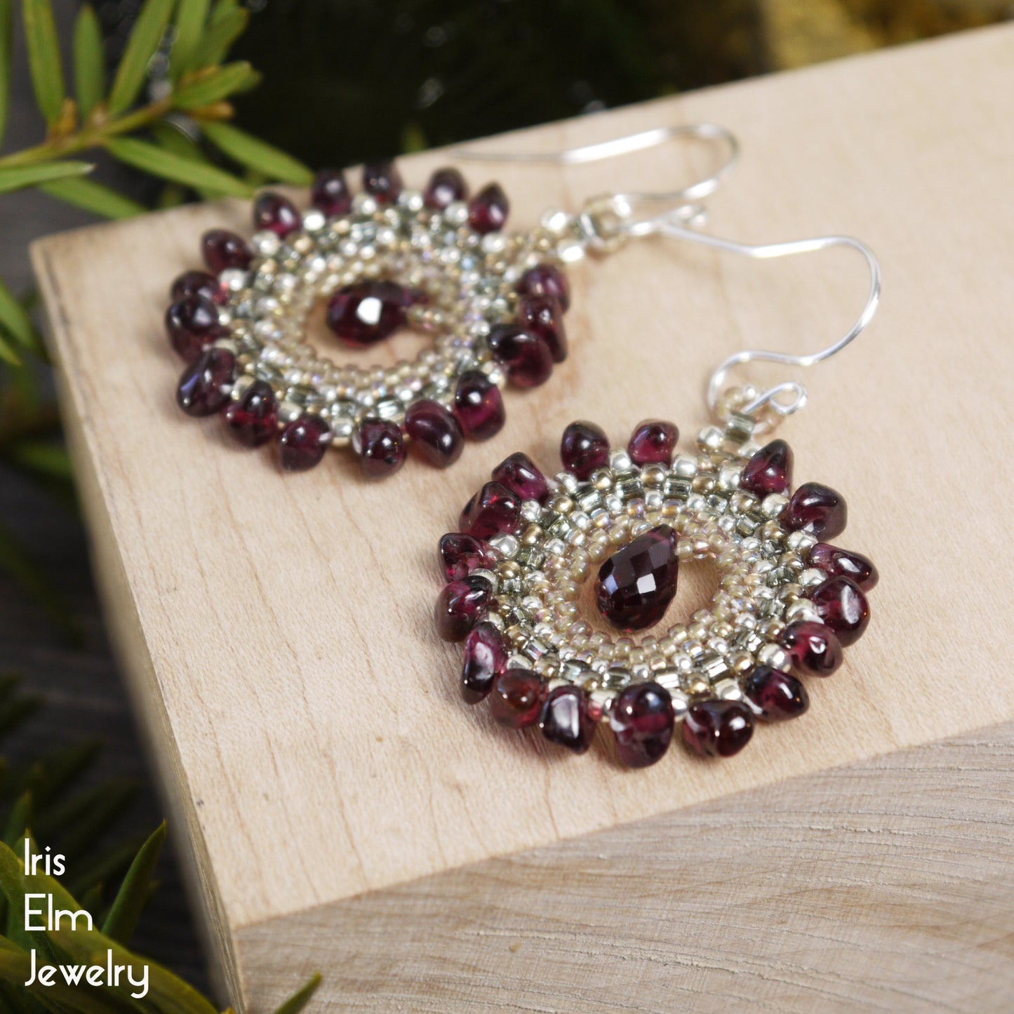 a pair of deep red garnet boho beadwork earrings on wooden block