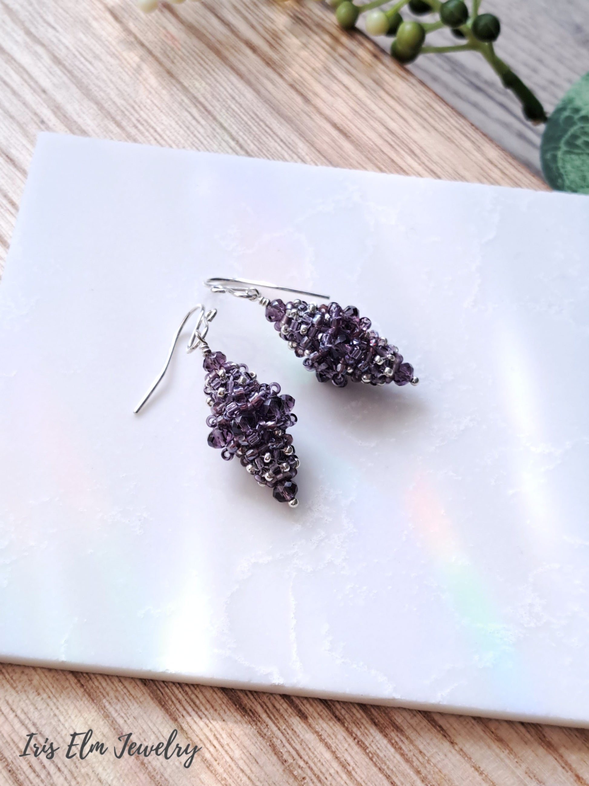 Pair of purple beaded bead glass earrings on a white marble surface with 'Iris Elm Jewelry' branding.