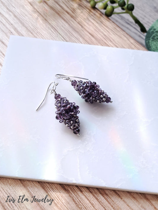 Pair of purple beaded bead glass earrings on a white marble surface with 'Iris Elm Jewelry' branding.