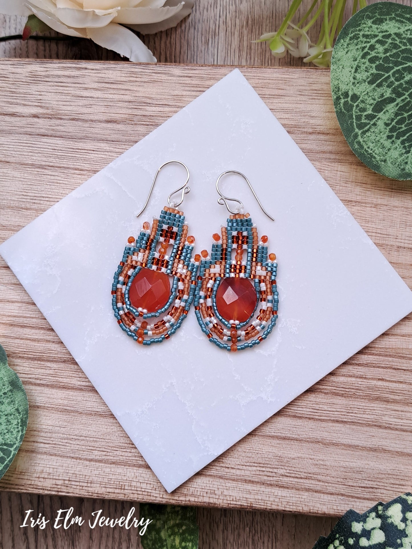 Beaded earrings with red orange carnelian stones on a white napkin with 'Iris Elm Jewelry' branding.