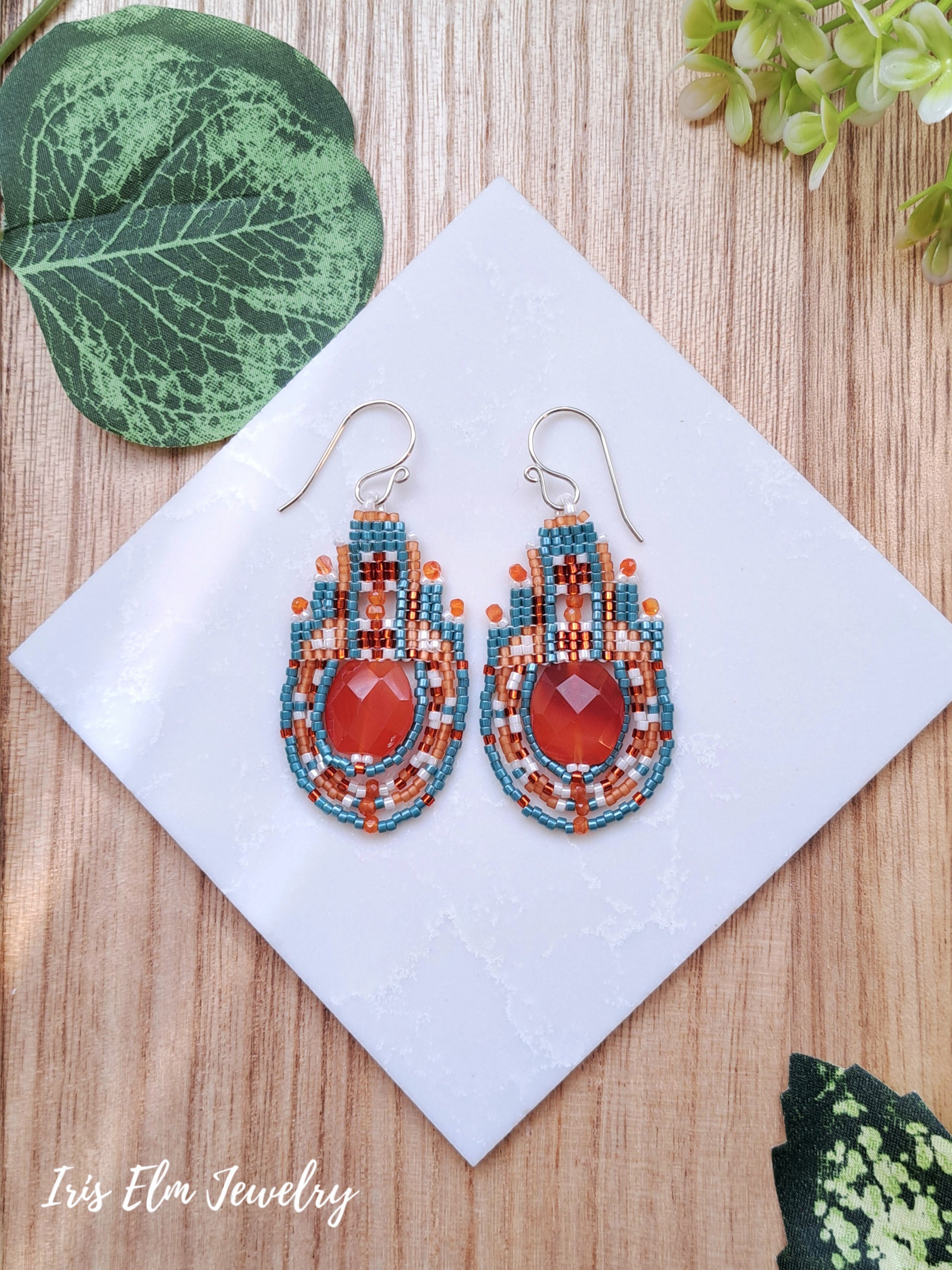 Colorful beaded carnelian gemstone earrings on a white square with green leaves in the background, featuring 'Iris Elm Jewelry'