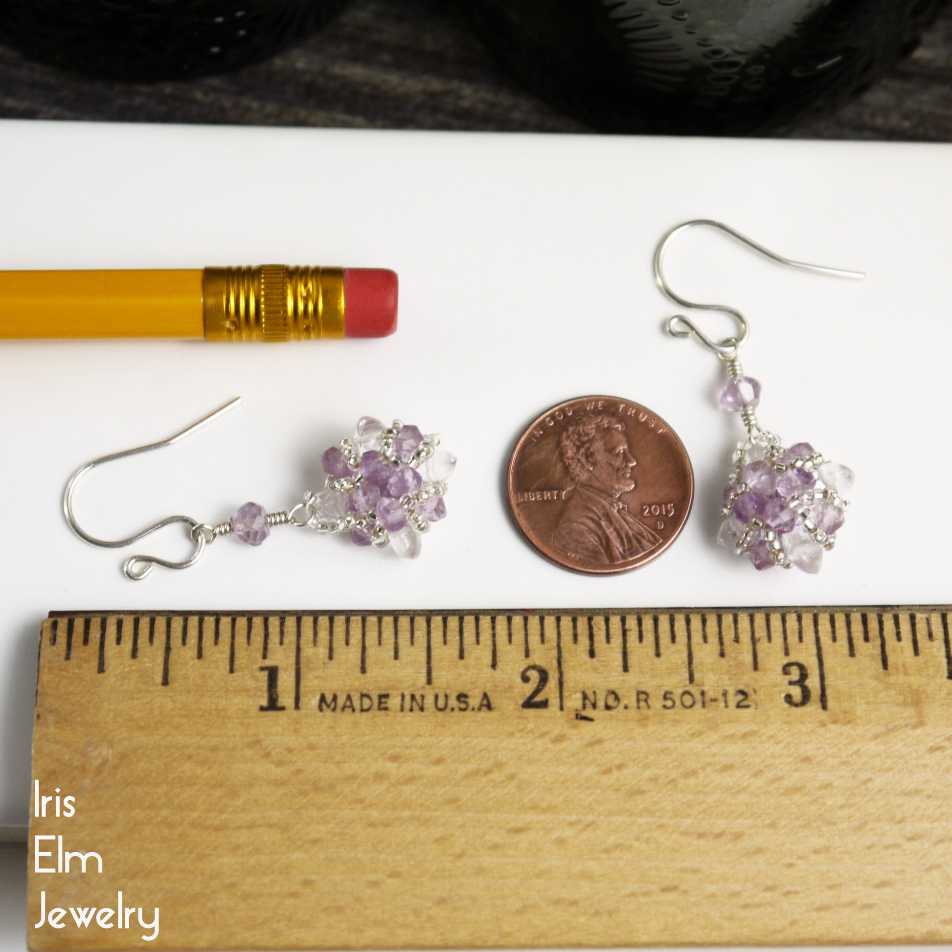 Pair of 1.5 inch long silver earrings with purple beads on a white surface with a penny and ruler for scale, featuring 'Iris Elm Jewelry'.