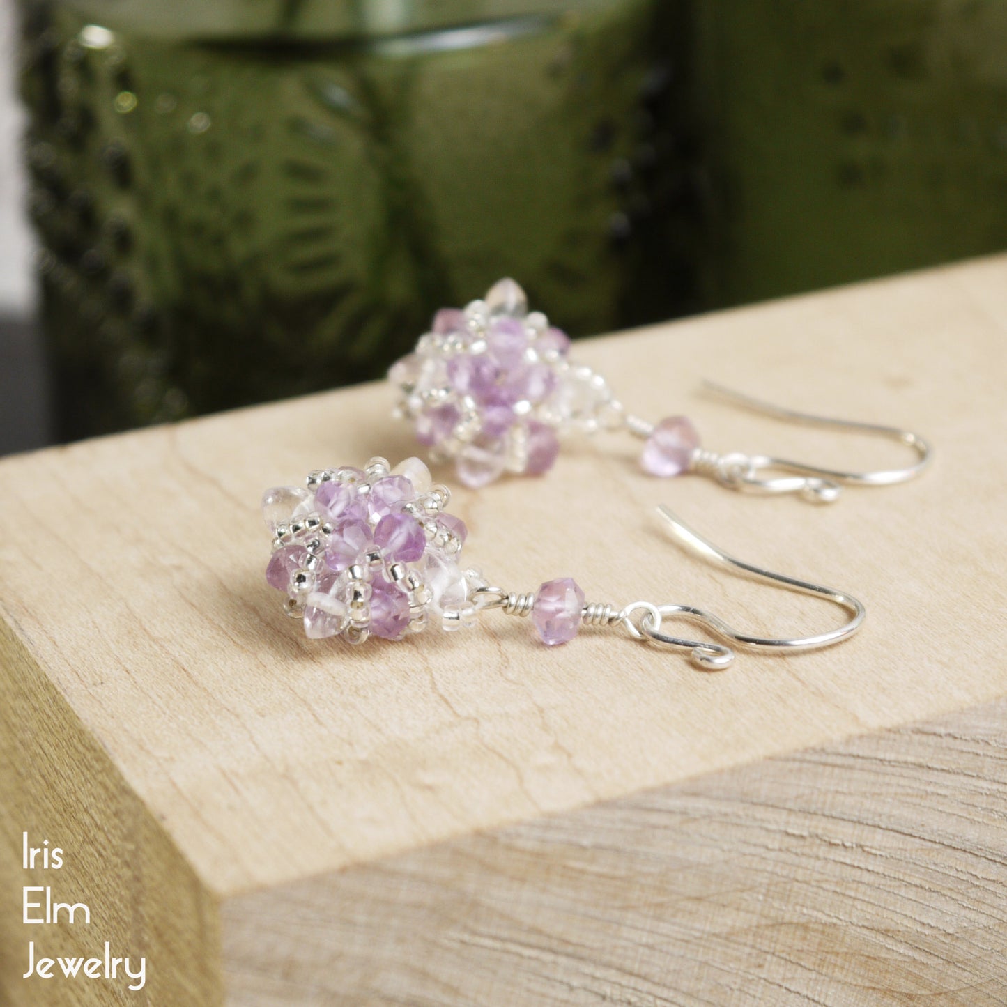 Pair of purple beaded amethyst and clear quartz crystal earrings on a wooden surface with 'Iris Elm Jewelry' branding.