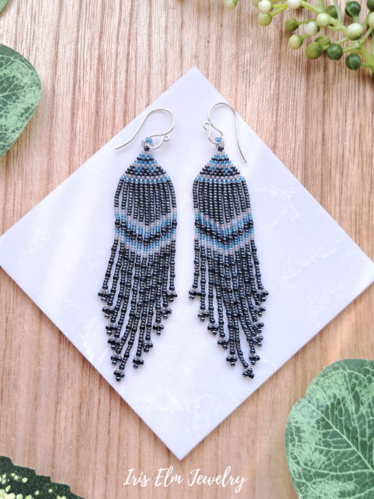 charcoal grey glass seed bead fringe handmade earrings on white tile surround by greenery with Iris Elm Jewelry branding