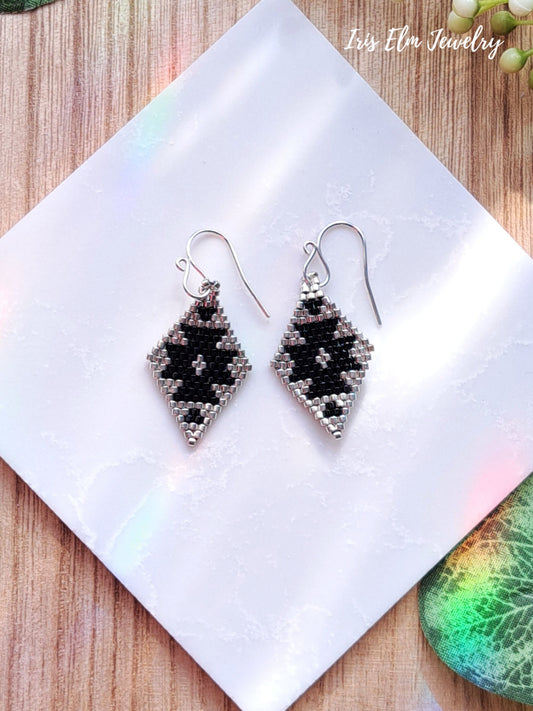 Pair of beaded black and silver seed bead diamond shape earrings on a white tile with 'Iris Elm Jewelry' branding.
