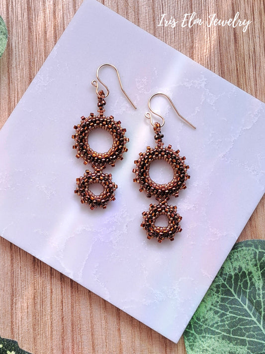 Pair of brown woven seed bead double hoop beaded earrings on a white card with 'Iris Elm Jewelry' branding.