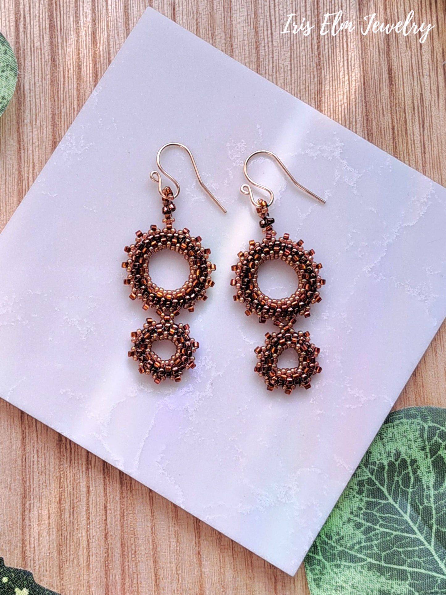 Pair of brown seed bead double hoop earrings on a white napkin with 'Iris Elm Jewelry' branding.