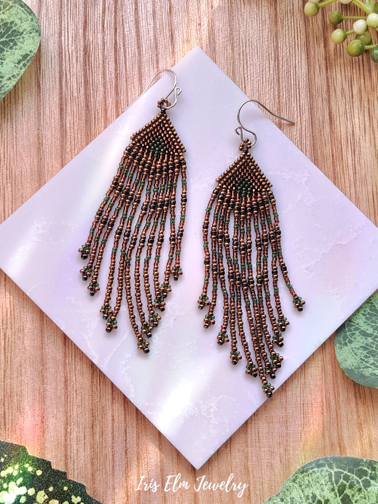 Beaded brown fringe seed bead earrings on a white square with 'Iris Elm Jewelry' branding, placed on a wooden surface.