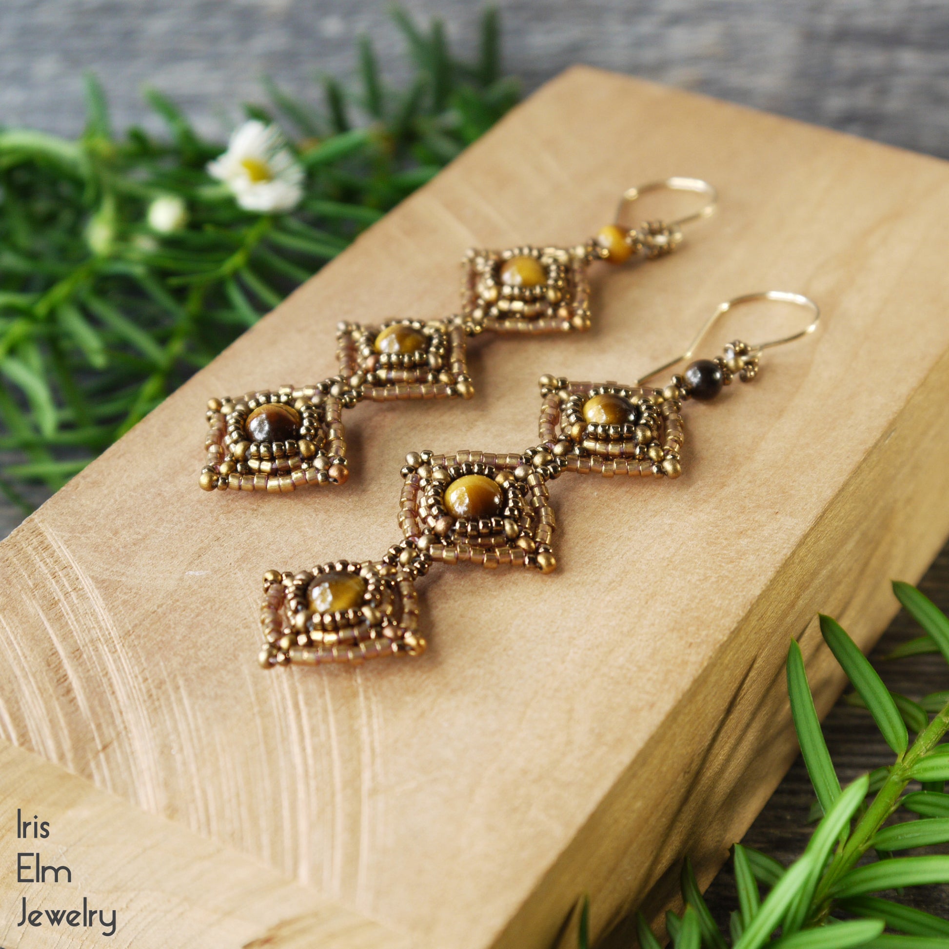 bronze seed bead beadwork earrings with tiger eye gemstones on a wooden surface with greenery