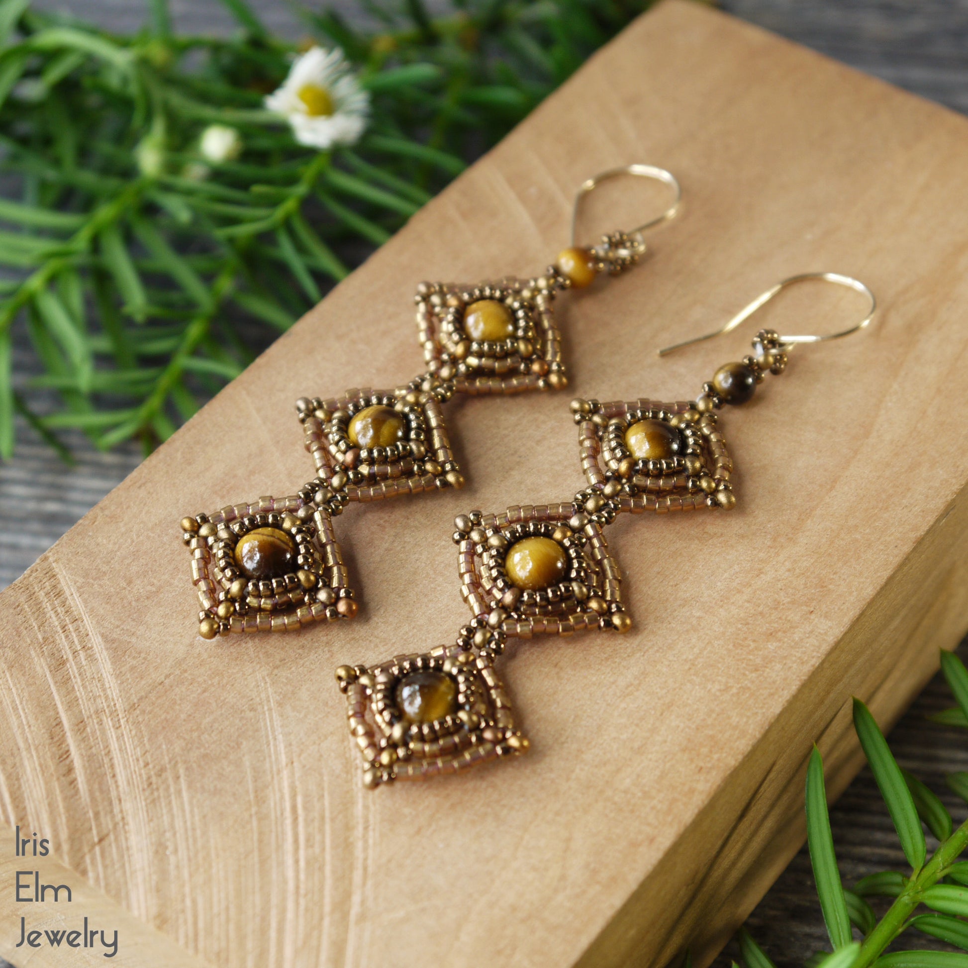 brown tiger eye beadwork long dangle handmade earrings with goldfilled ear wires on a wooden surface with greenery.