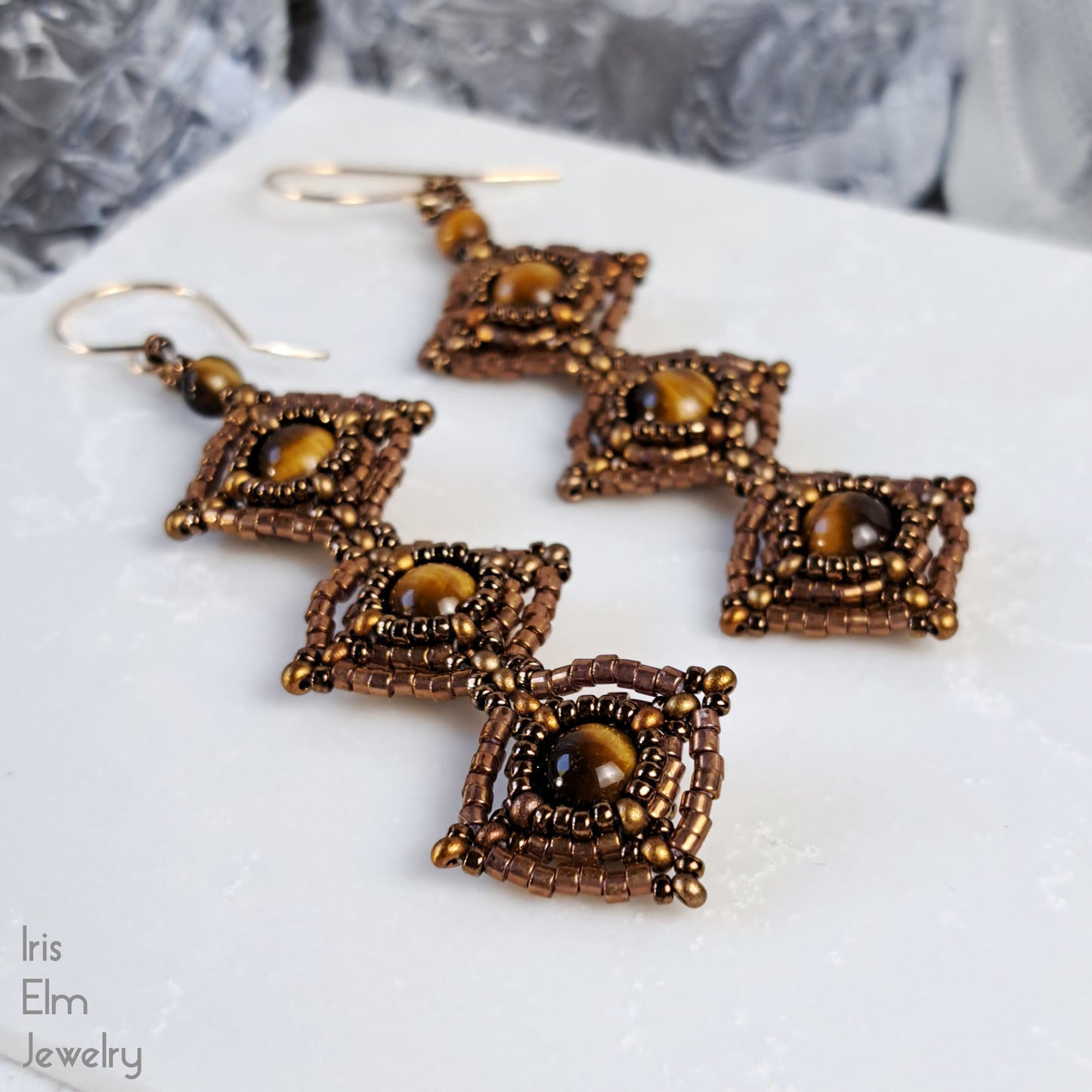 Pair of bronze-colored beaded earrings on a white surface with 'Iris Elm Jewelry' branding.