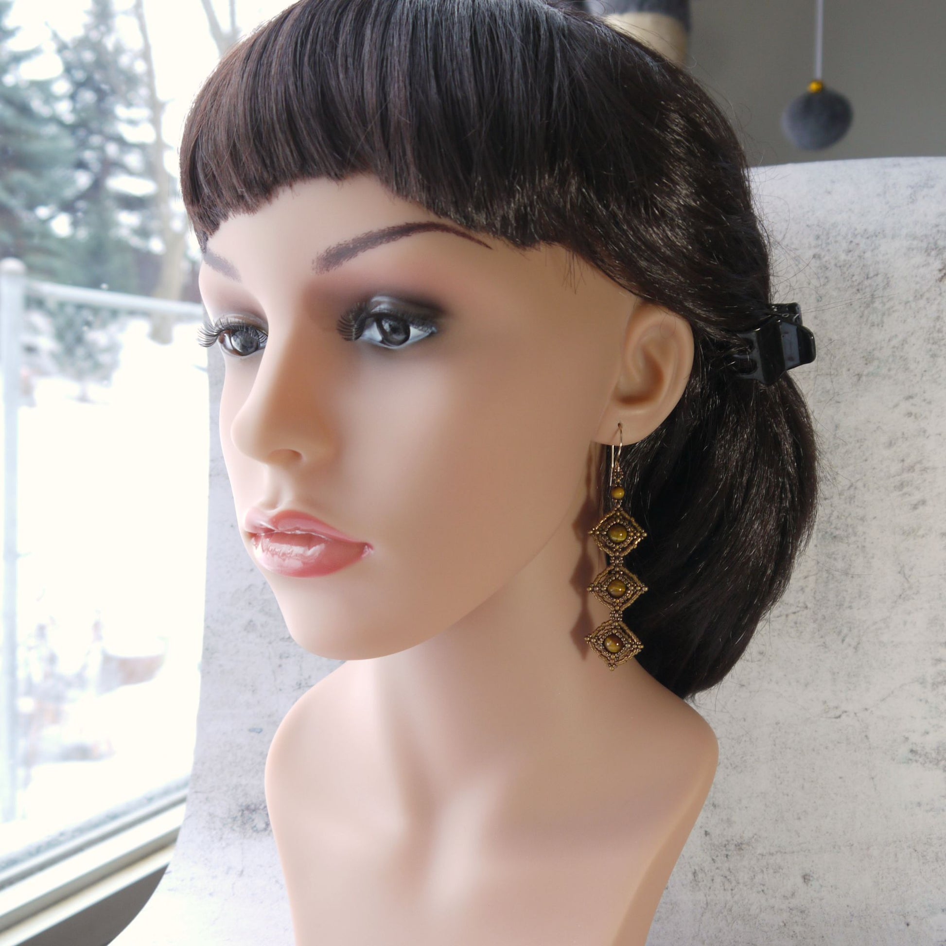 Mannequin head with dark hair styled in a bun, wearing long tiger eye earrings.