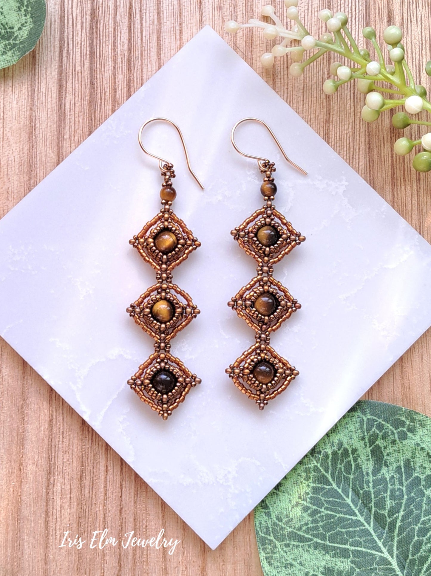Pair of intricate long beadwork tiger eye earrings on a white square with a natural background