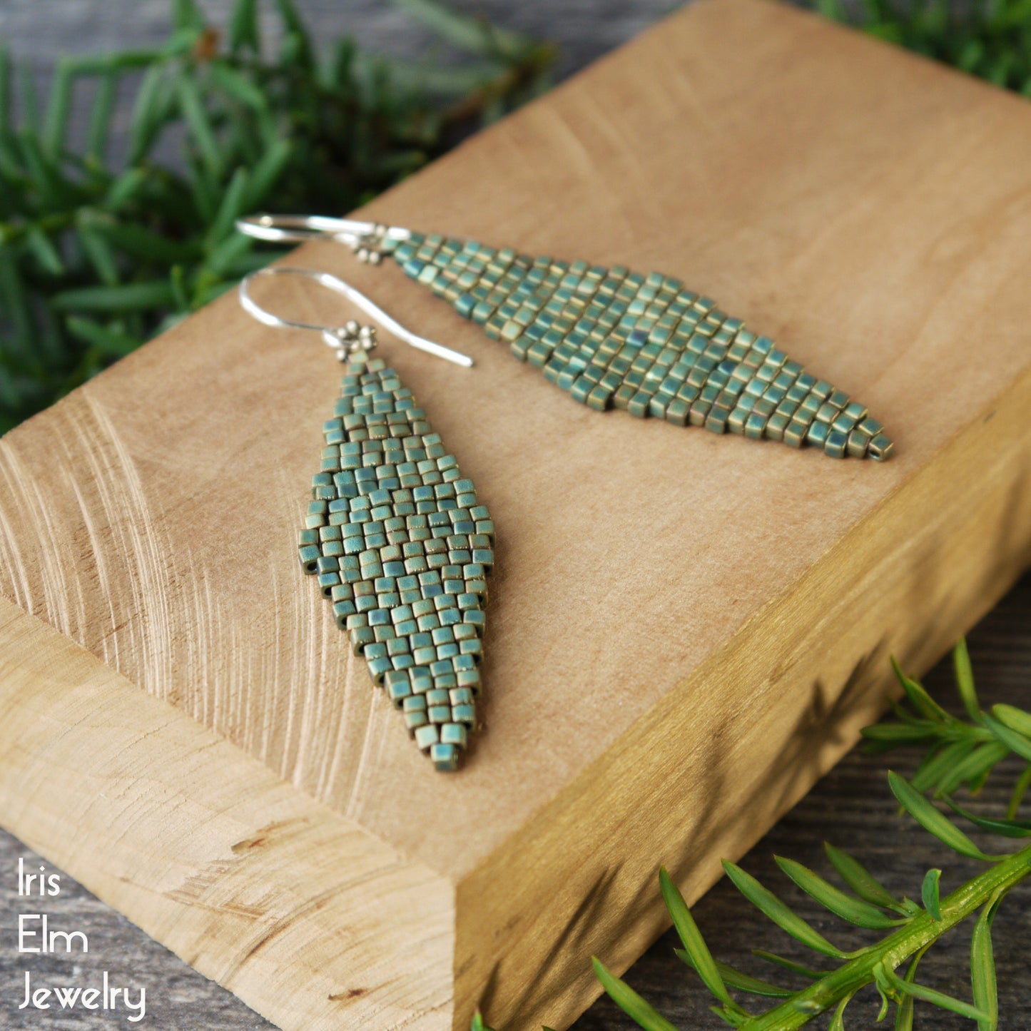 Turquoise mettalic matte glass beaded earrings with sterling silver ear wires on a wooden block with greenery in the background