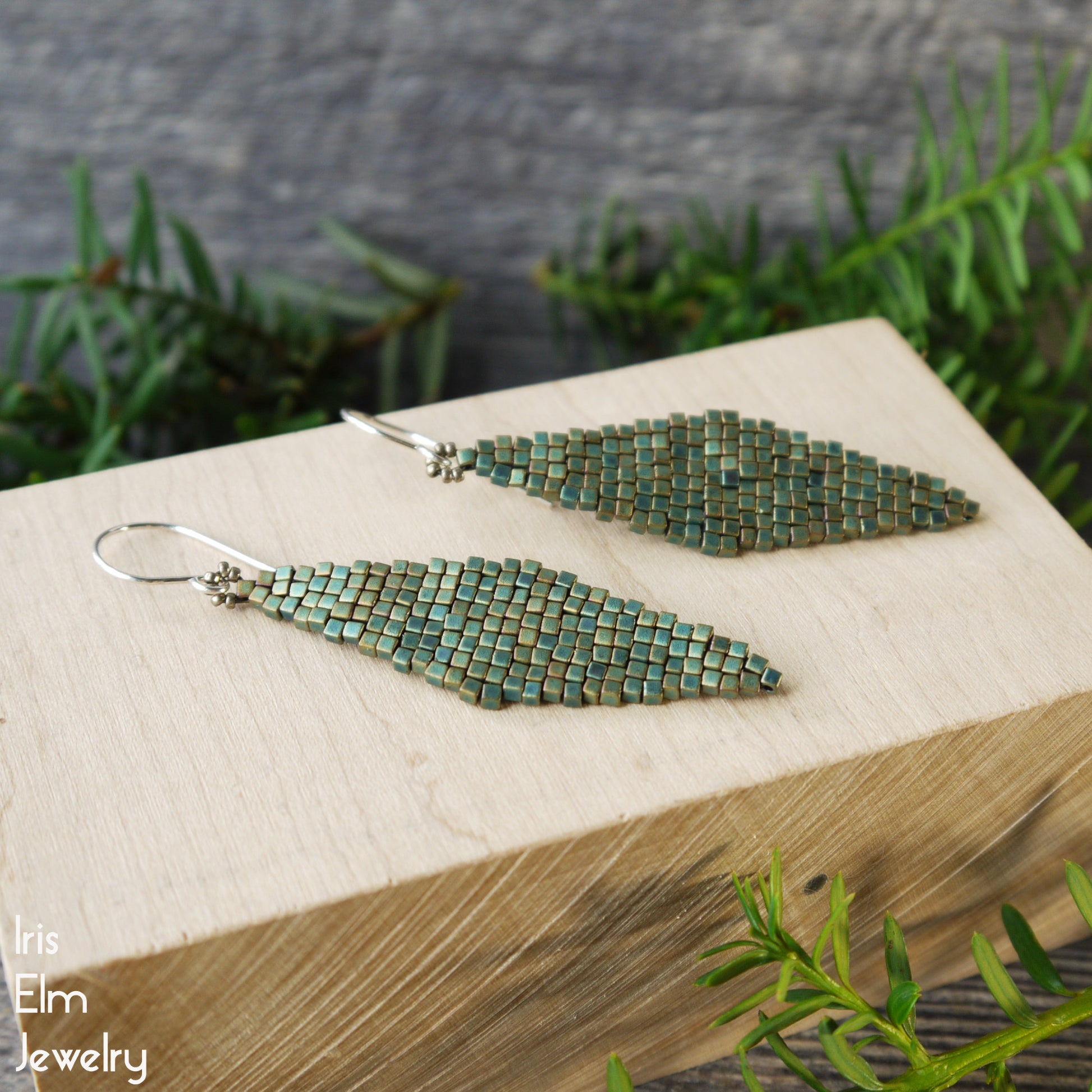 turquoise Green beaded glass long dangle earrings on a wooden block with a natural background