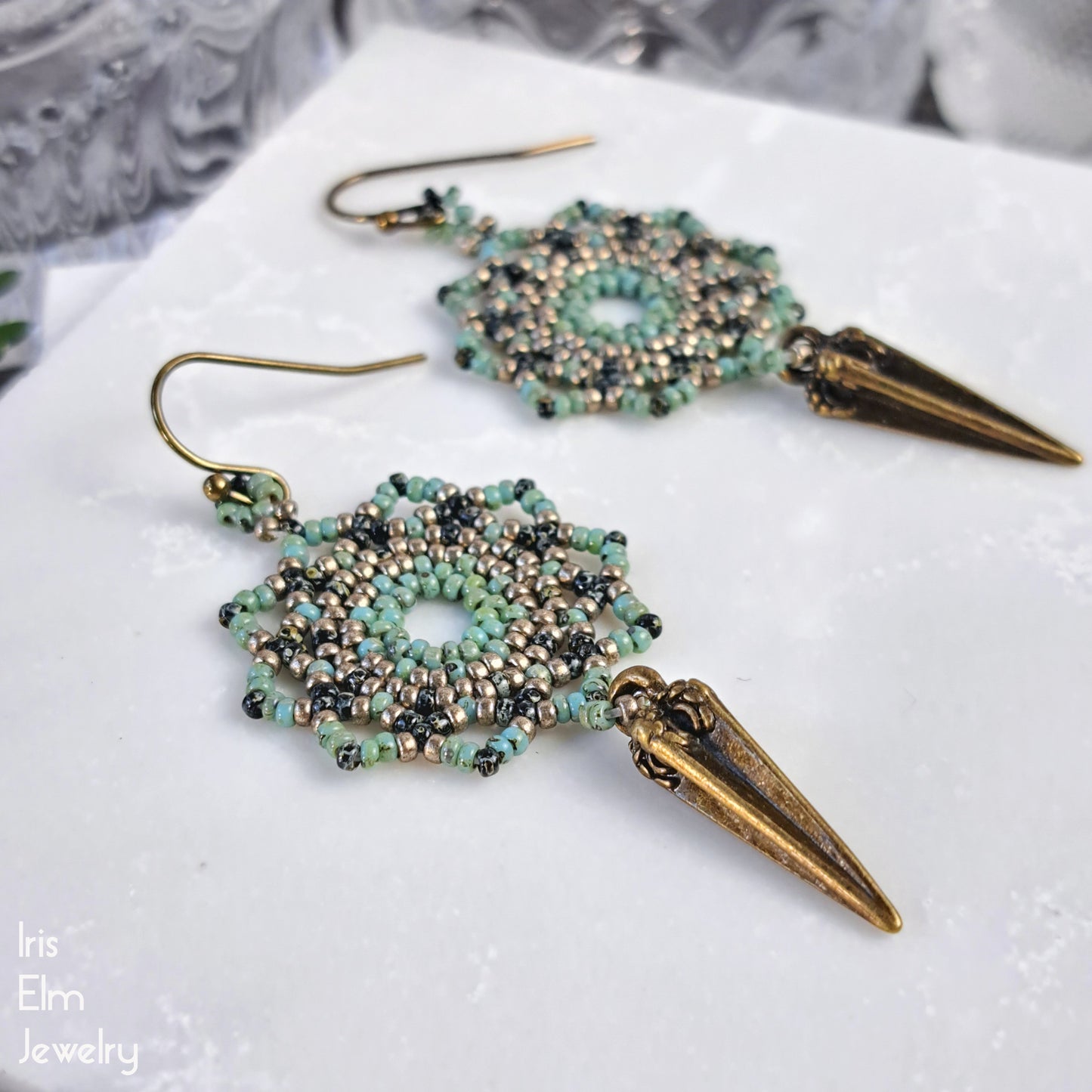 green glass Beaded mandala earrings with brass spike details on a white surface, featuring 'Iris Elm Jewelry' branding.