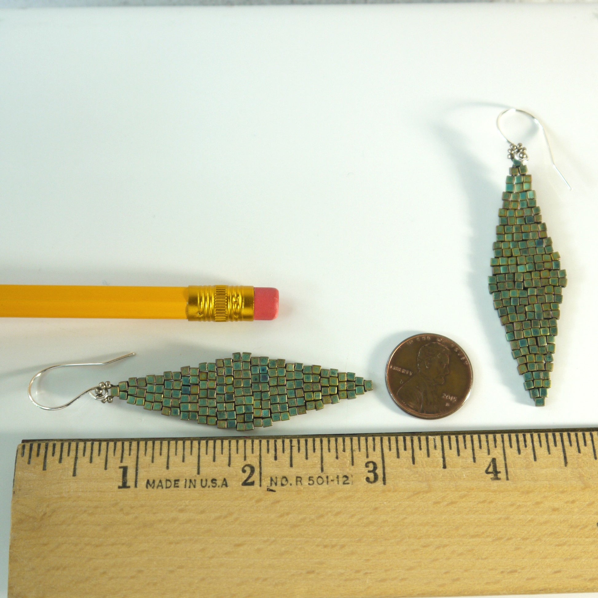 2 and 7/8 inches long Green beaded earrings next to a pencil and coin on a white background with a ruler for scale.