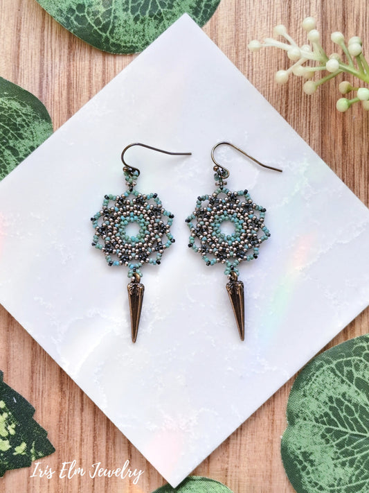 Pair of seed bead mandala and spike earrings on a white napkin with green leaves in the background