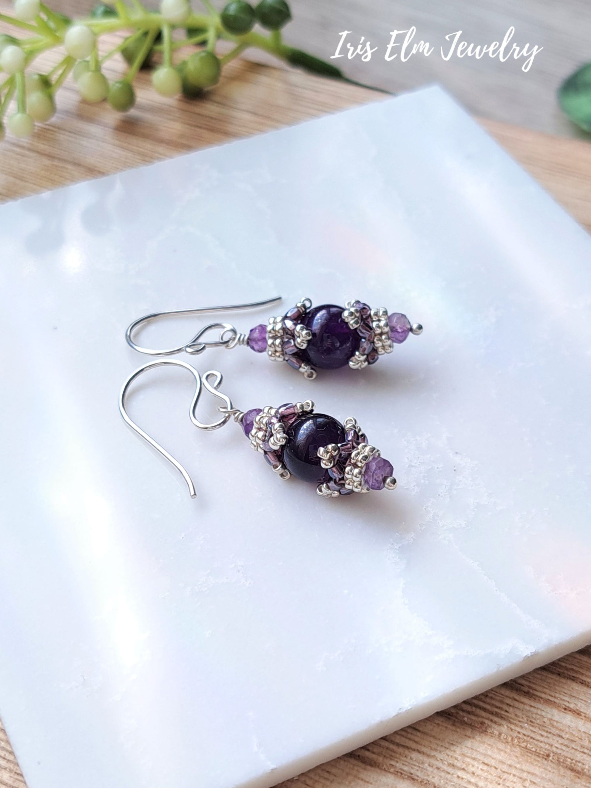 small dark purple amethyst sterling silver drop earrings on white marble surface with Iris Elm Jewelry branding.