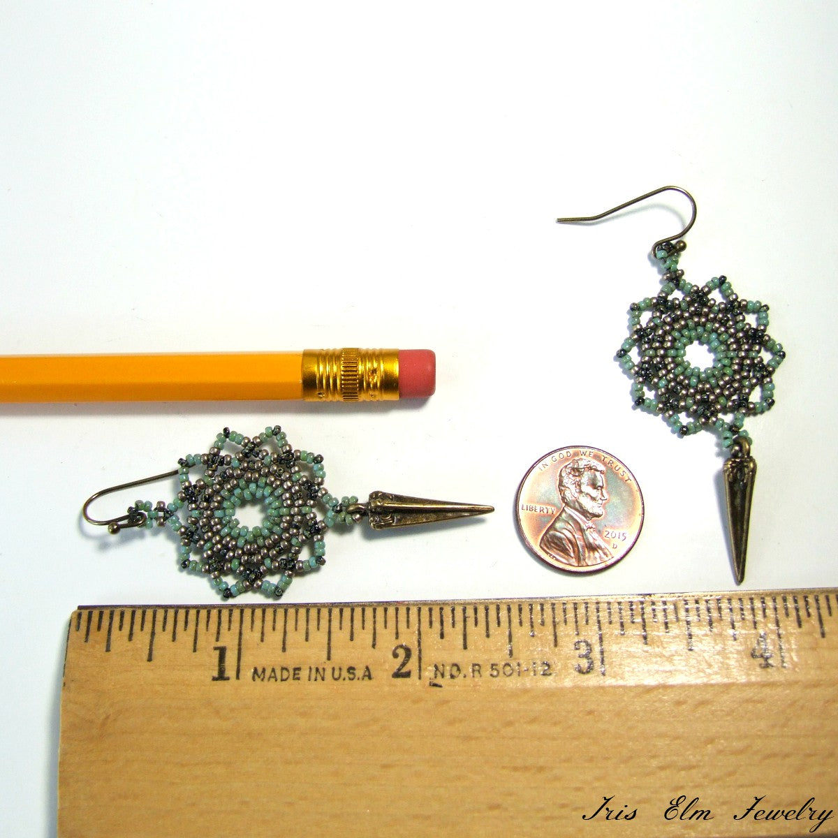 Pair of green mandala spike beaded earrings with a pencil and penny for scale on a white background