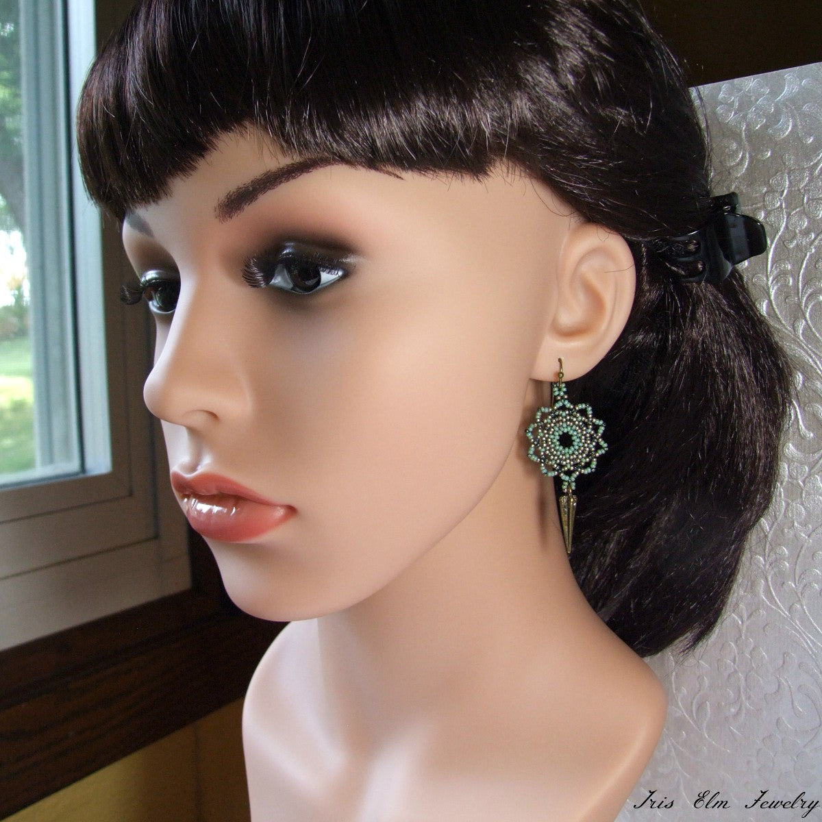 Mannequin head with dark hair and green mandala earrings against a neutral background