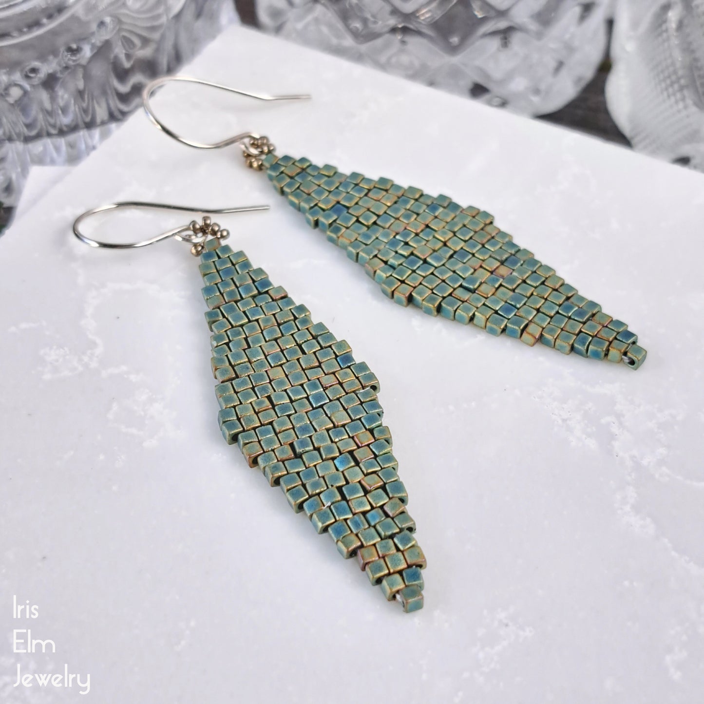 Pair of teal beaded diamond shape matte glass earrings on a textured white surface with 'Iris Elm Jewelry' branding.