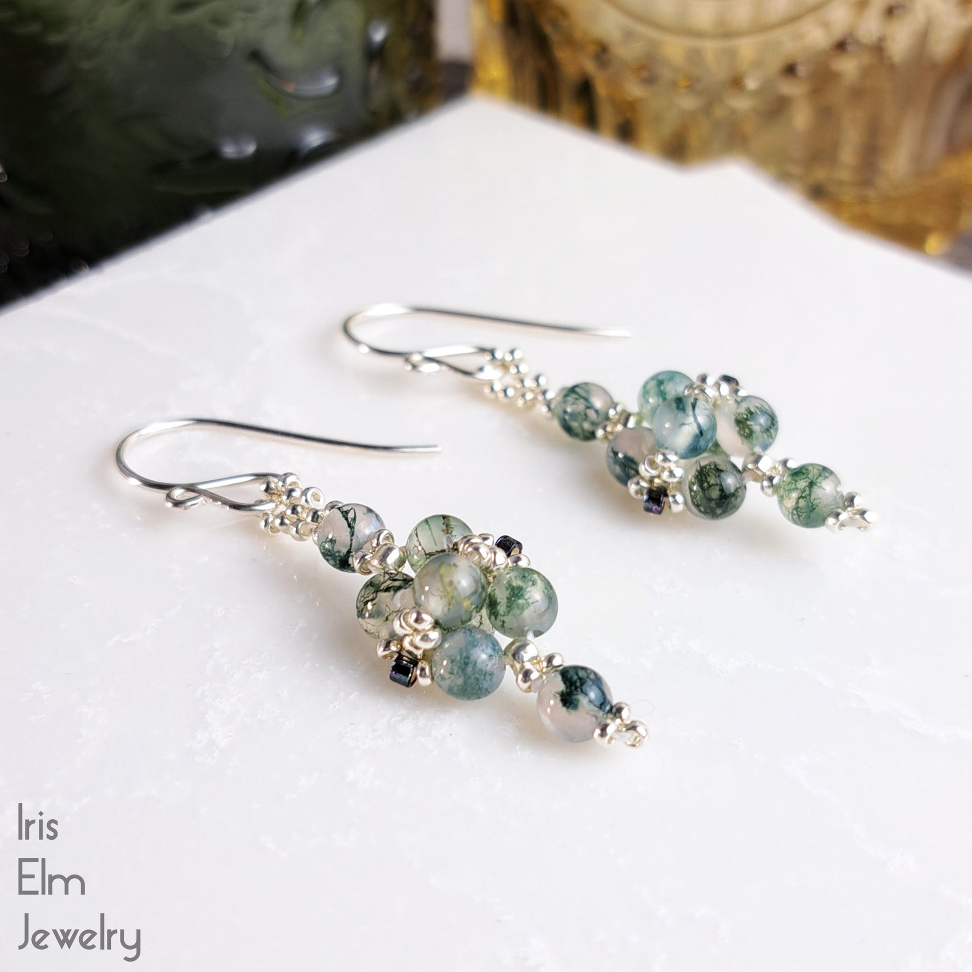 Pair of green moss agate beaded handmade earrings with sterling silver ear wires on a white surface with 'Iris Elm Jewelry' branding.