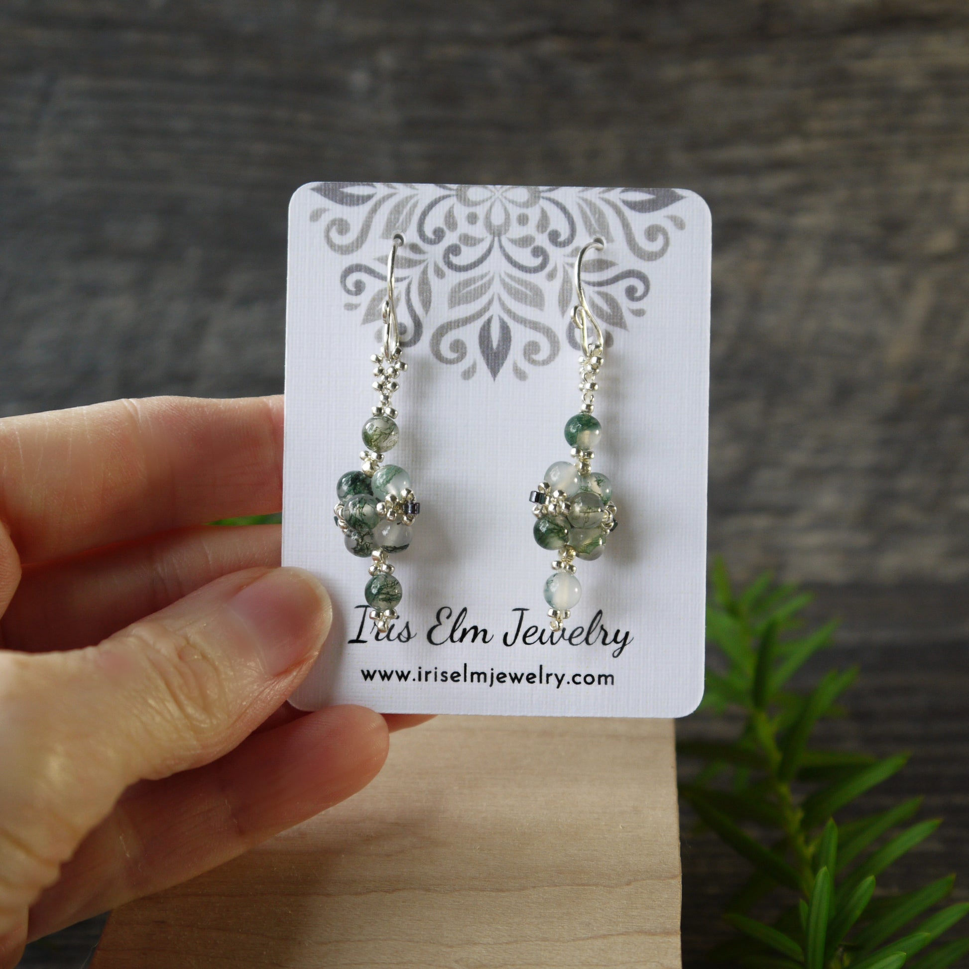 Green moss agate beaded earrings on a card held by a hand with a natural background