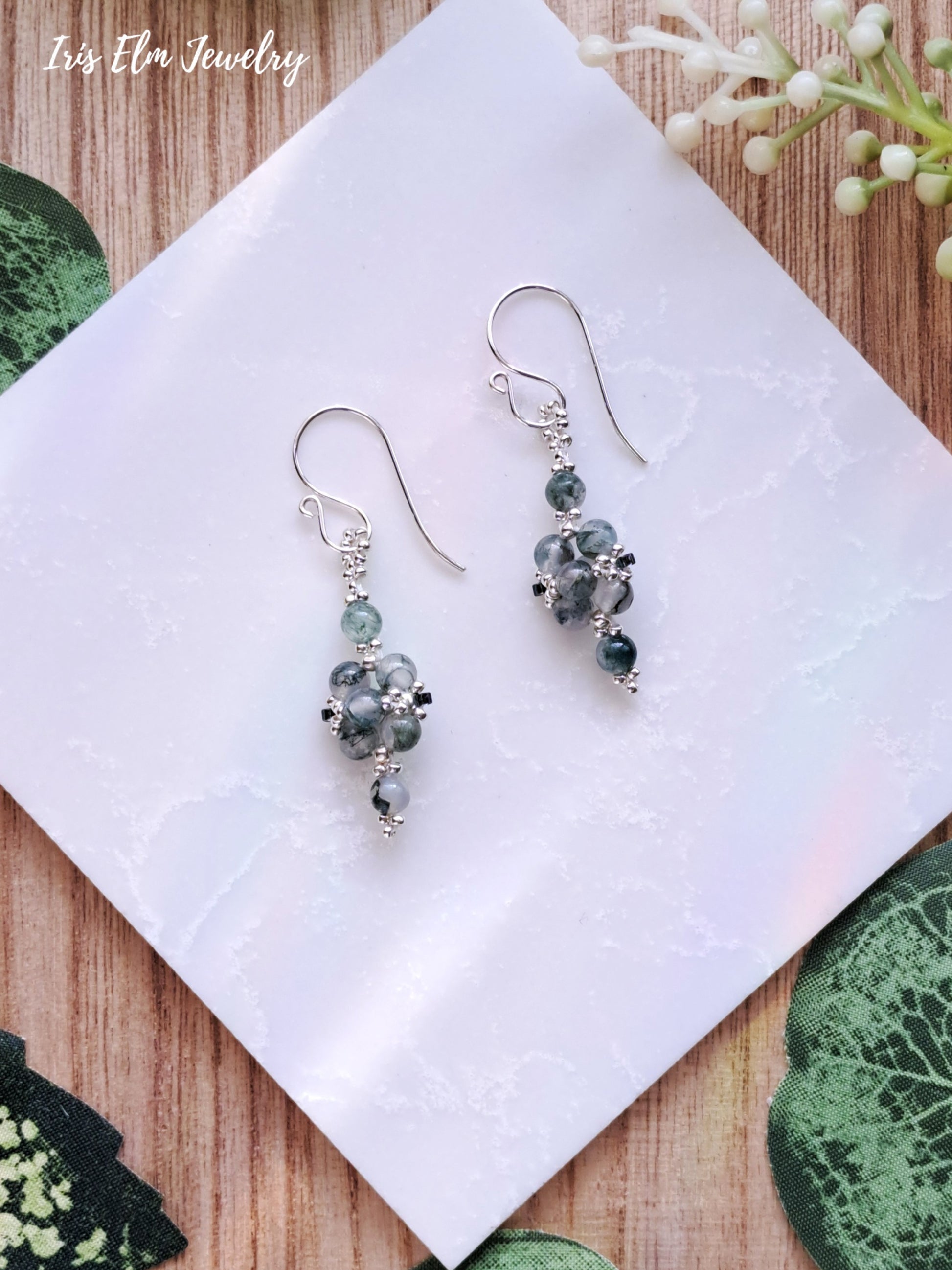 Silver earrings with green moss agate stone beads on a white tile, branded 'Iris Elm Jewelry'.