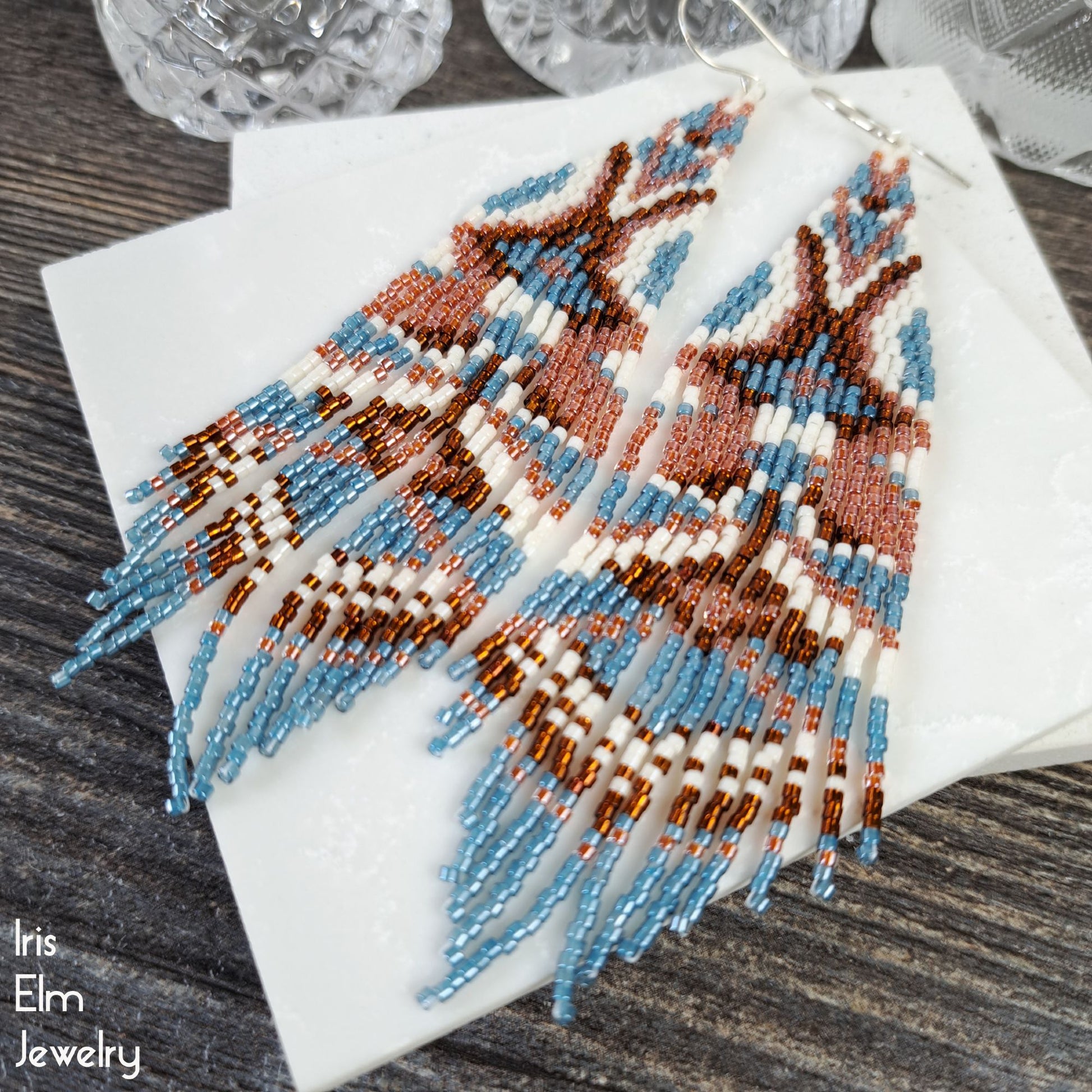 Beaded long fringe seed bead earrings with blue and brown patterns on a white stone surface