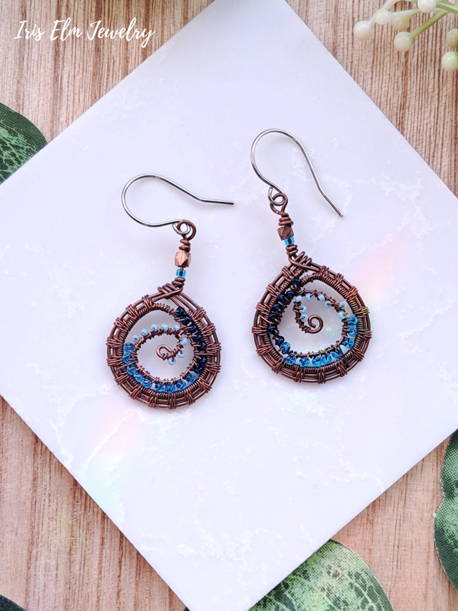 Pair of spiral copper wire wrapped earrings on a white card with a wooden background