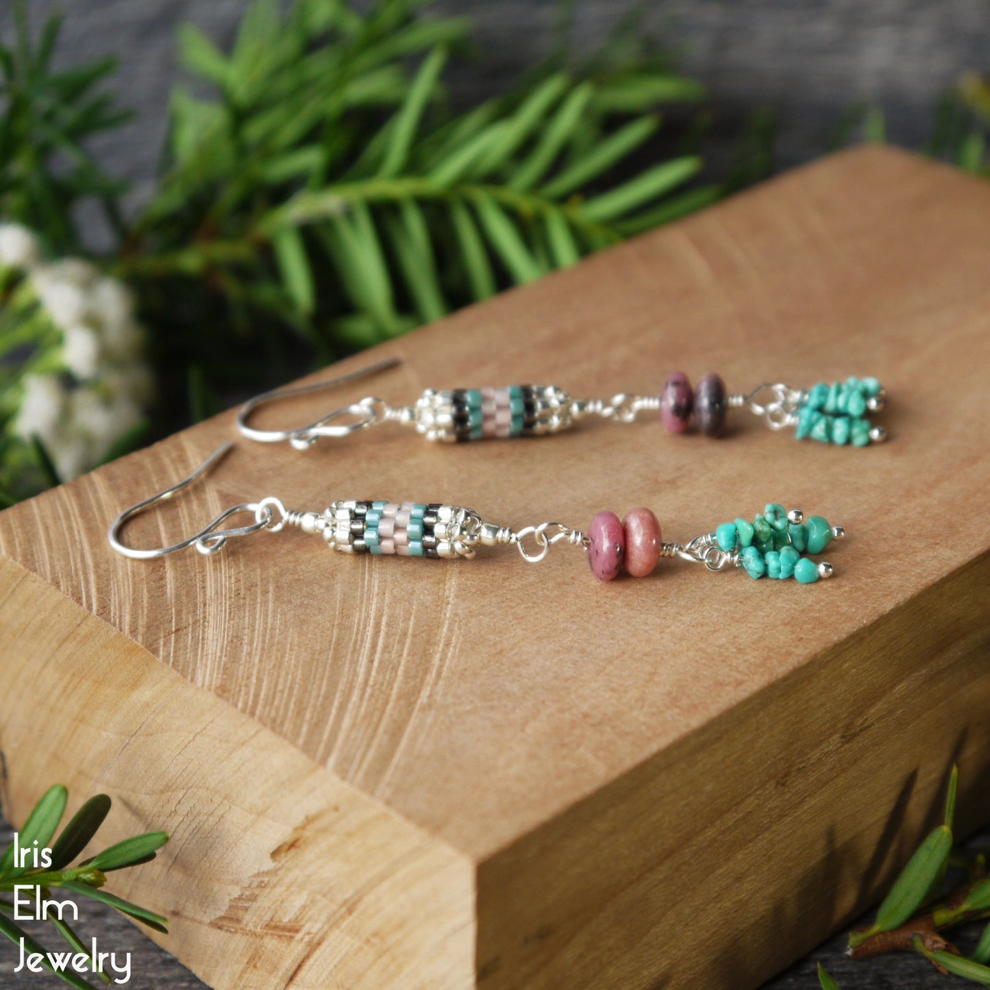 Beaded rhodonite and turquoise with seed bead beadwork dangle earrings on a wooden block with 'Iris Elm Jewelry' branding.