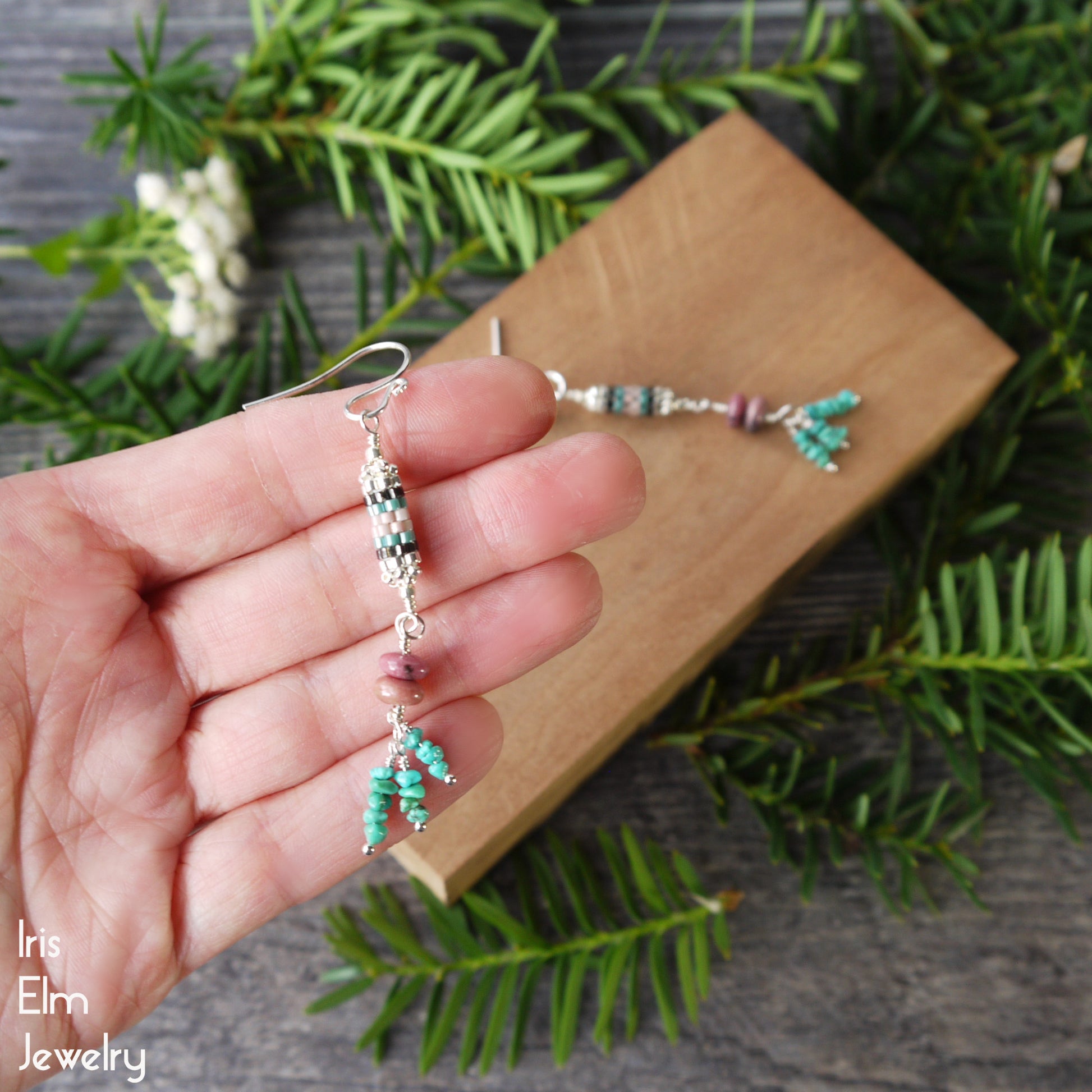 Hand holding a pair of turquoise and pink rhodonite sterling silver beaded earrings with a natural background