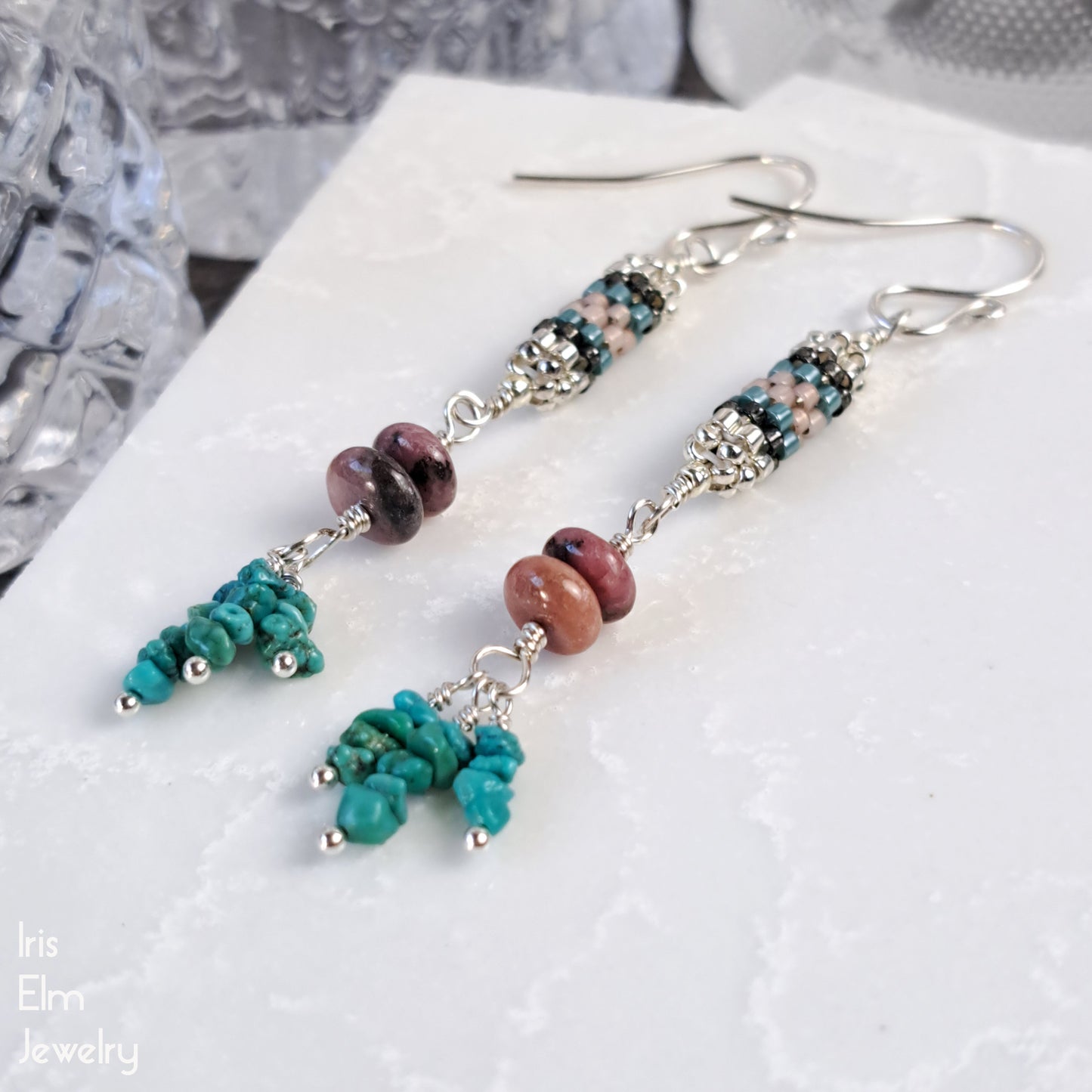 Pair of handmade beaded earrings with turquoise and pink stone beads with cylindrical seed bead beadwork on a white surface.