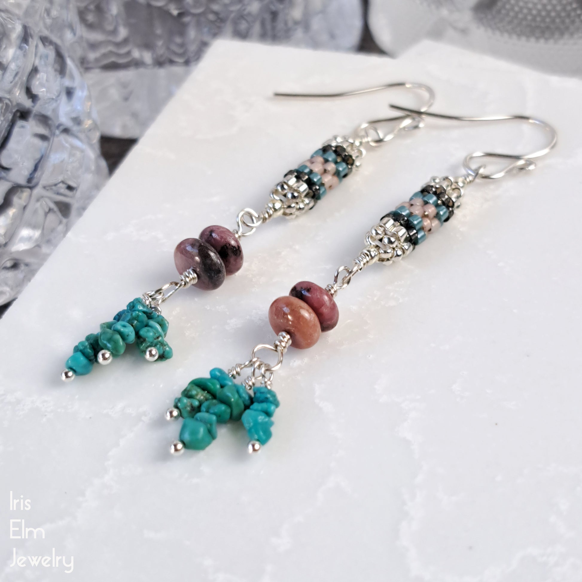 Pair of handmade beaded earrings with turquoise and pink stone beads with cylindrical seed bead beadwork on a white surface.