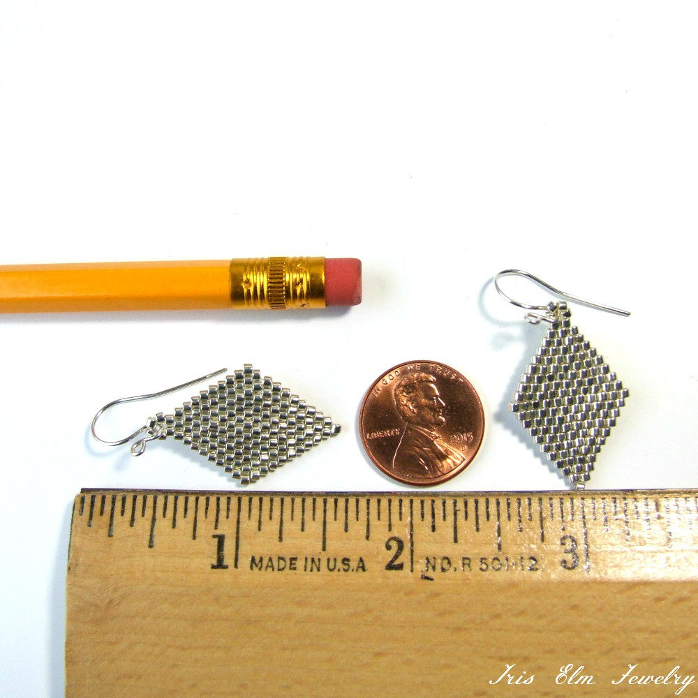 Small silver seed bead diamond shape earrings next to a penny and ruler for scale on a white background