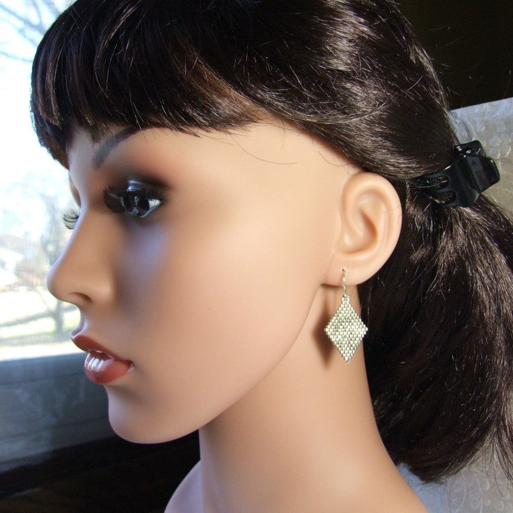 Mannequin head with dark hair tied back and wearing a silver diamond-shaped earring.