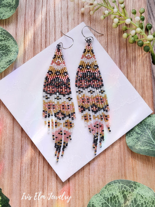 Pair of beaded pink grey white yellow seed bead fringe earrings on a white card with green leaves around