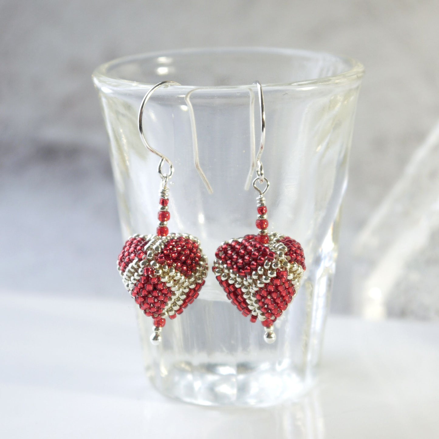 triangle-shaped beaded drop earrings on a clear glass with a white background