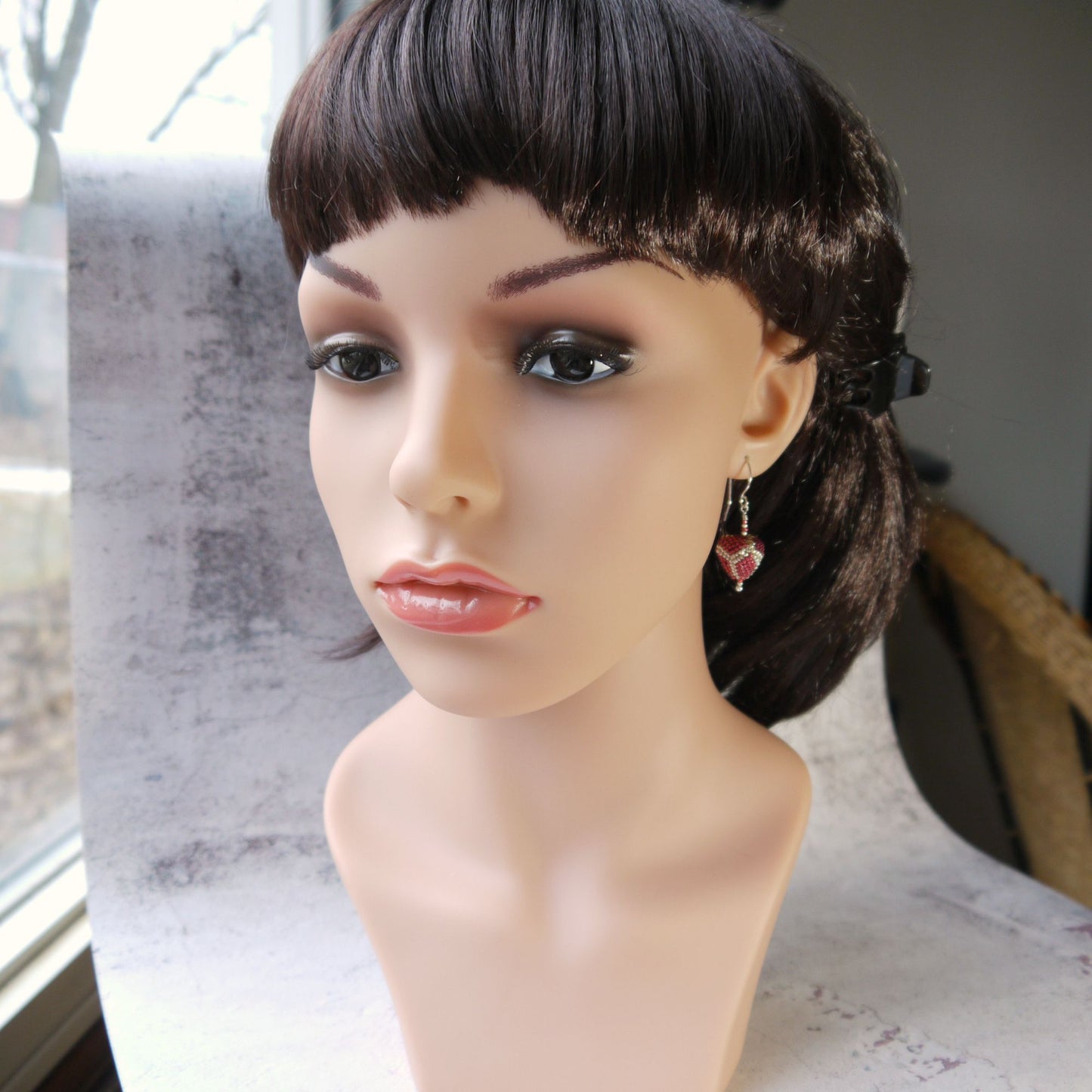 Mannequin head with a short black wig wearing red triangle drop earrings on a blurred indoor background