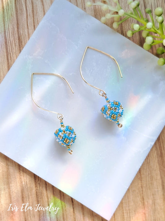 light blue, gold, white small seed bead triangle drop earrings on white marble surface with Iris Elm Jewelry branding.