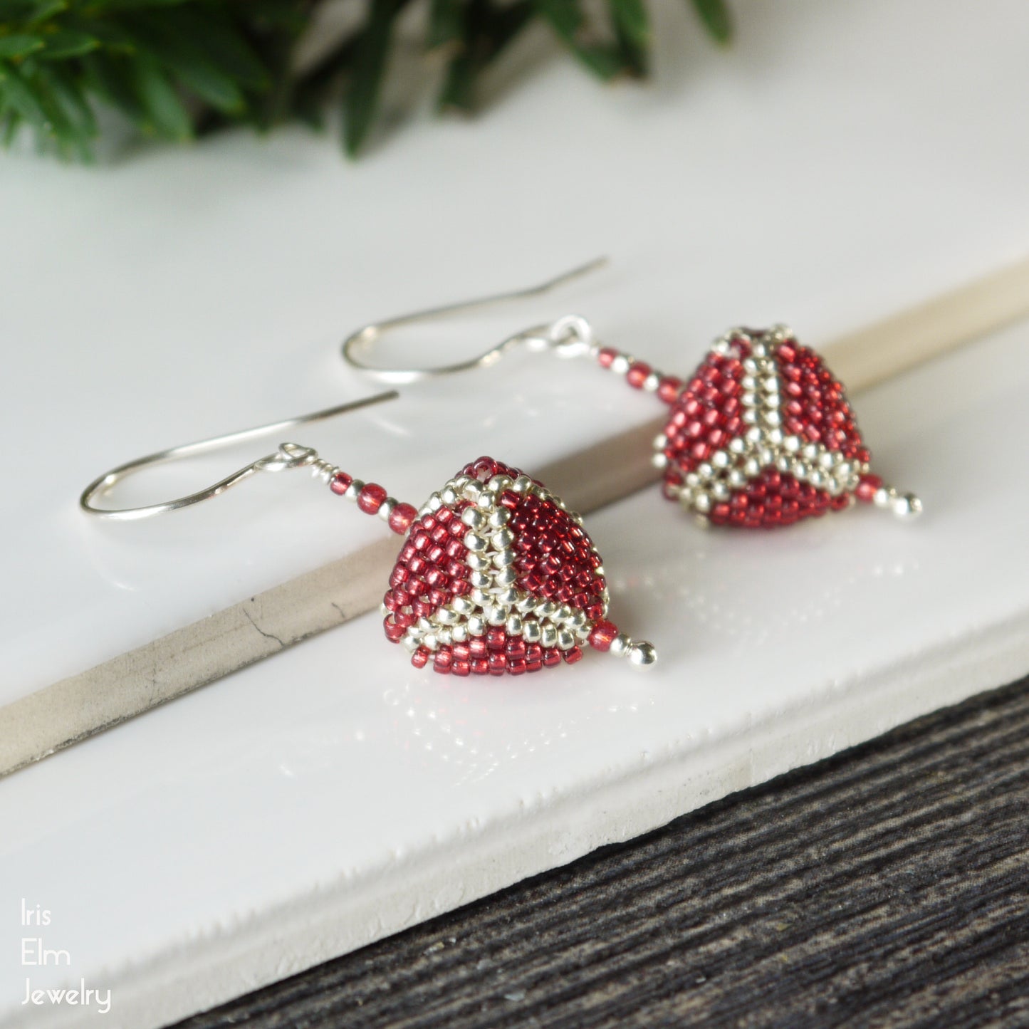 Beaded red and silver triangle seed bead sterling silver earrings on a white surface with a blurred natural background