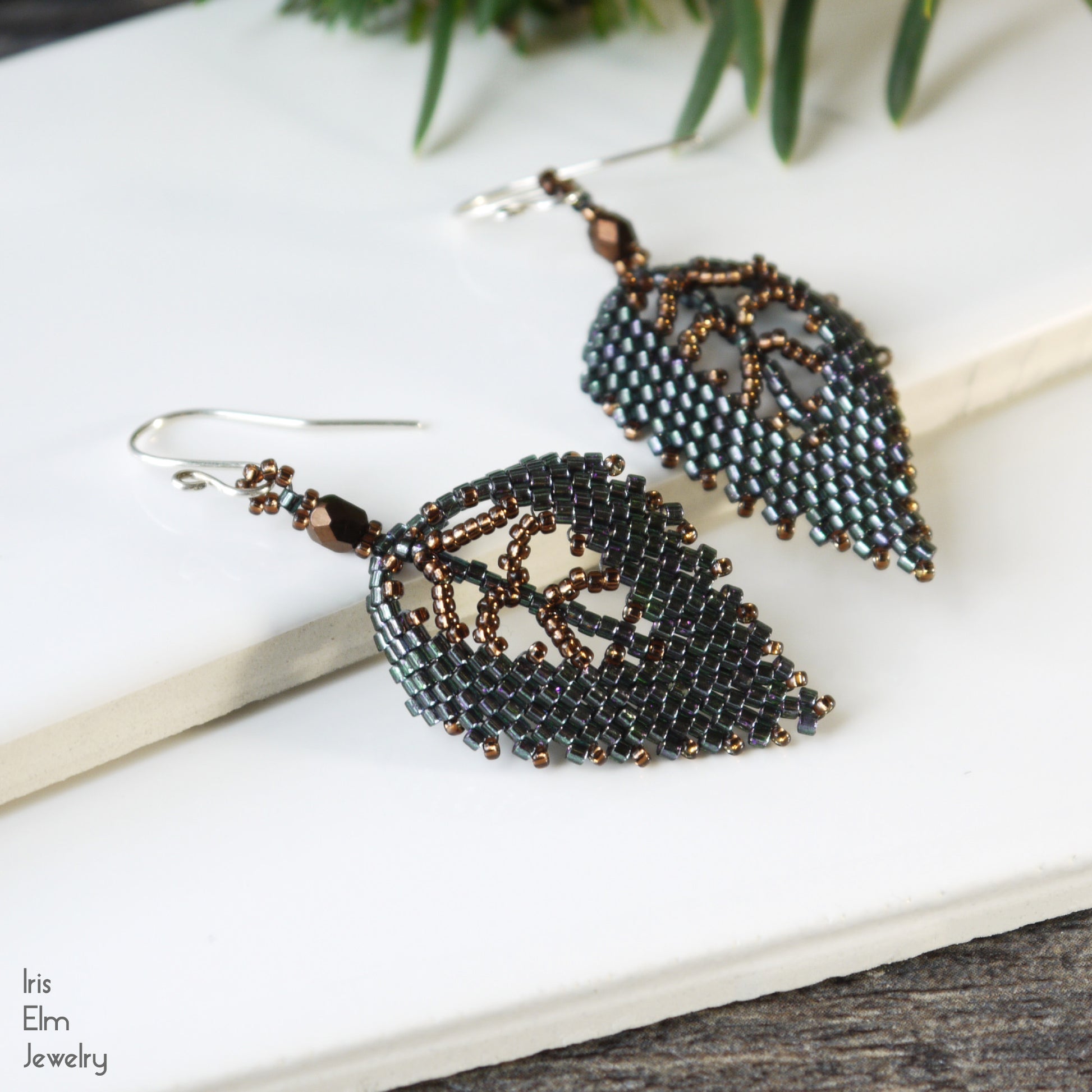 handmade woven Leaf-shaped beaded glass seed bead earrings on a white surface with 'Iris Elm Jewelry' branding.