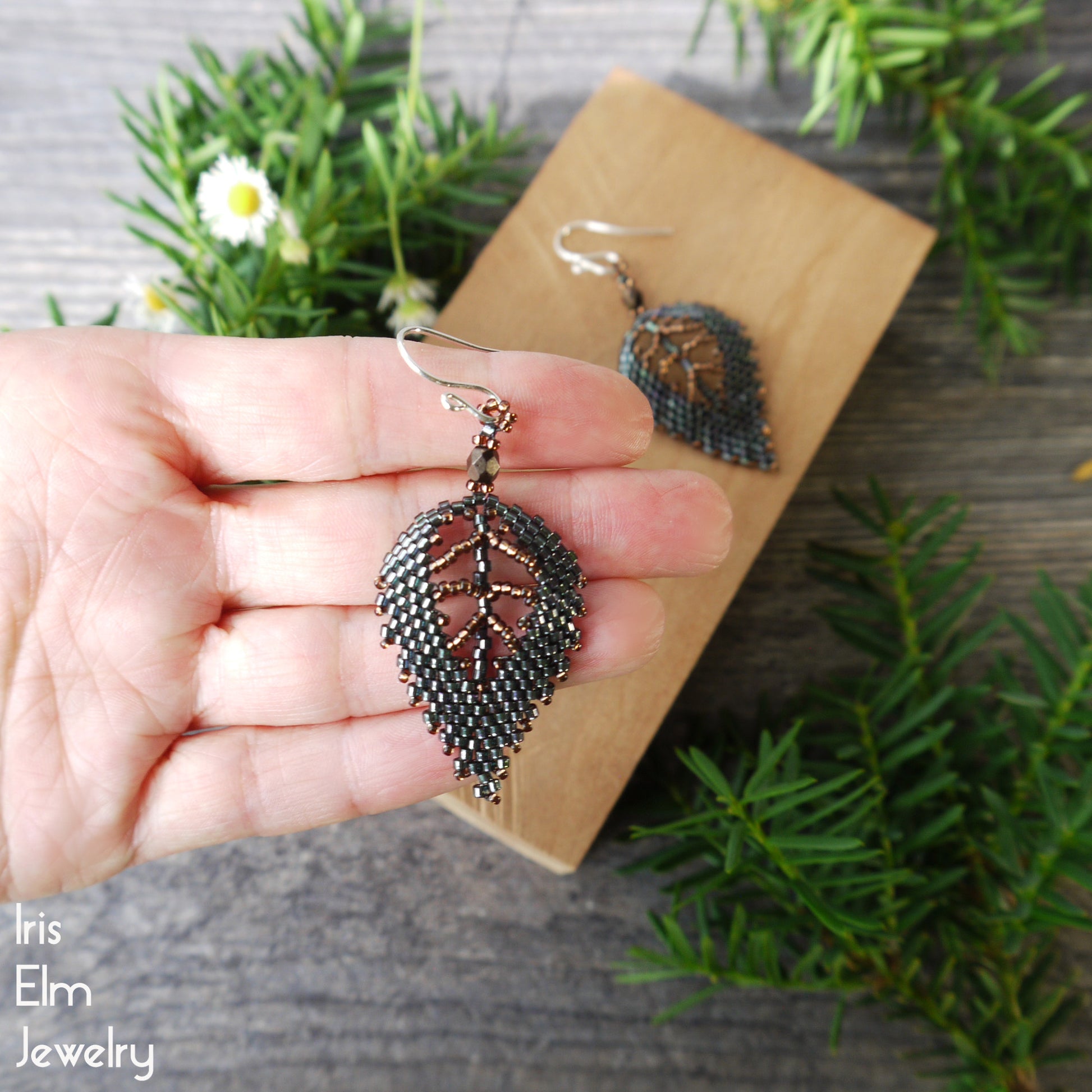 Leaf-shaped beaded green earrings held in a hand with a natural background