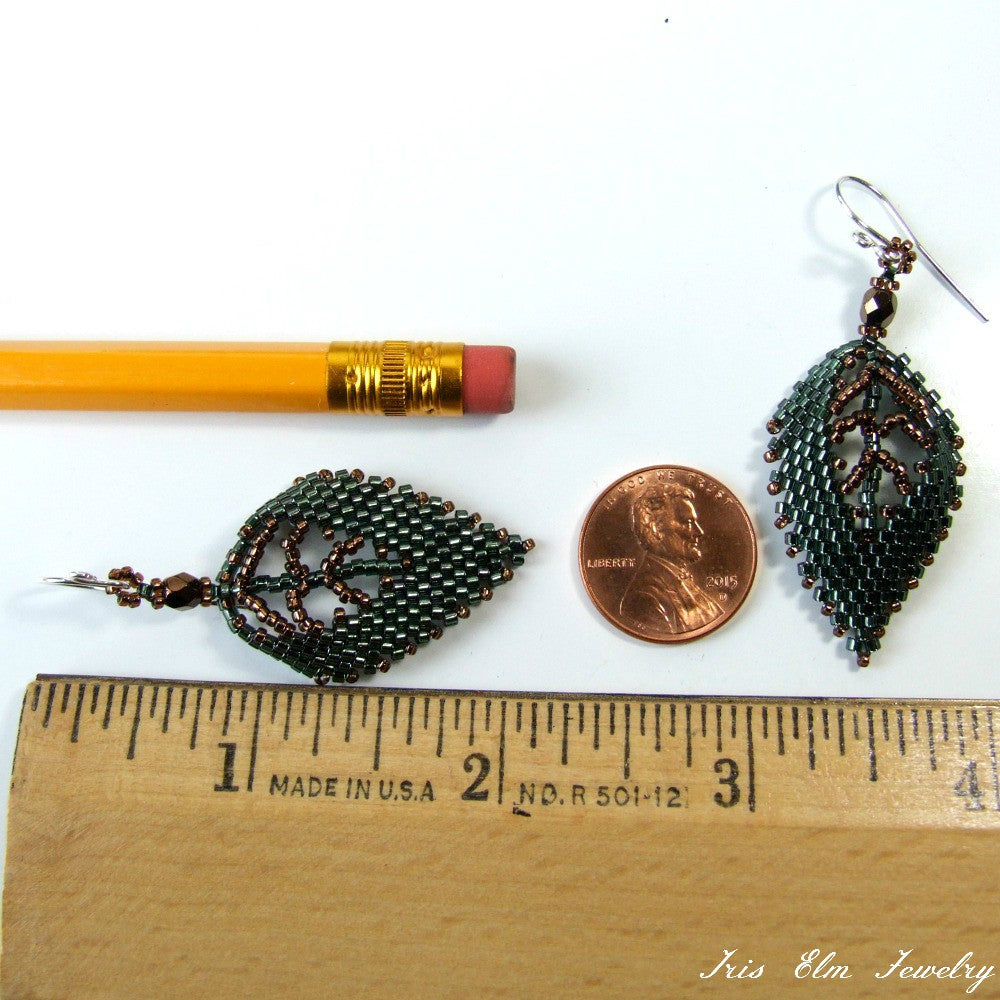 Leaf-shaped beaded seed bead earrings next to a pencil, penny, and ruler for scale on a white background.