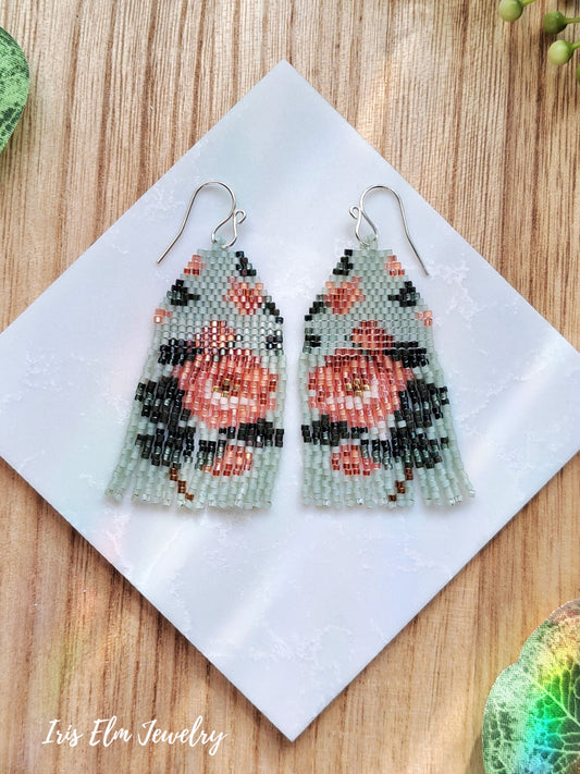 Pair of beaded mint green and peach rose floral seed bead fringe earrings on a white tile with 'Iris Elm Jewelry' branding.
