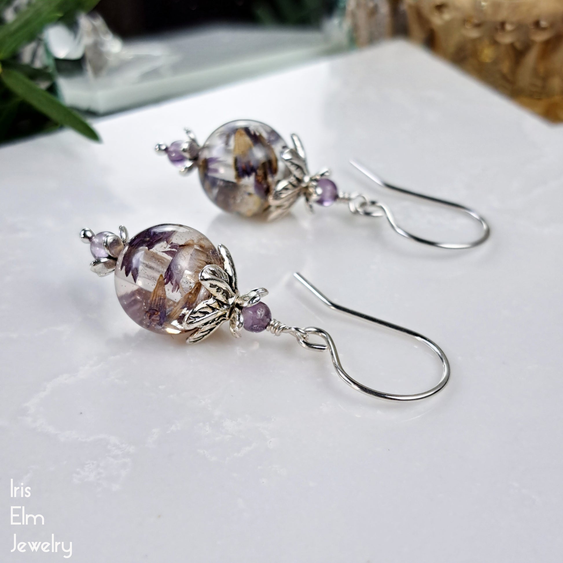 Pair of purple and silver beaded resin flower earrings on a white surface with 'Iris Elm Jewelry' branding.