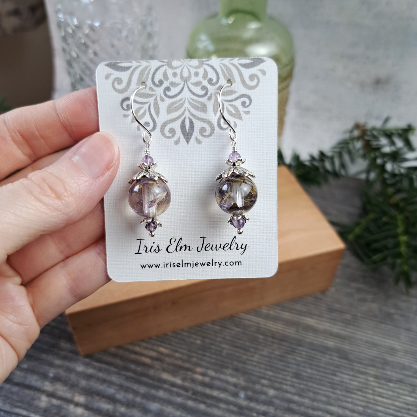 real flower with amethyst gemstone Earrings on a 'Iris Elm Jewelry' card held by a hand with a blurred background