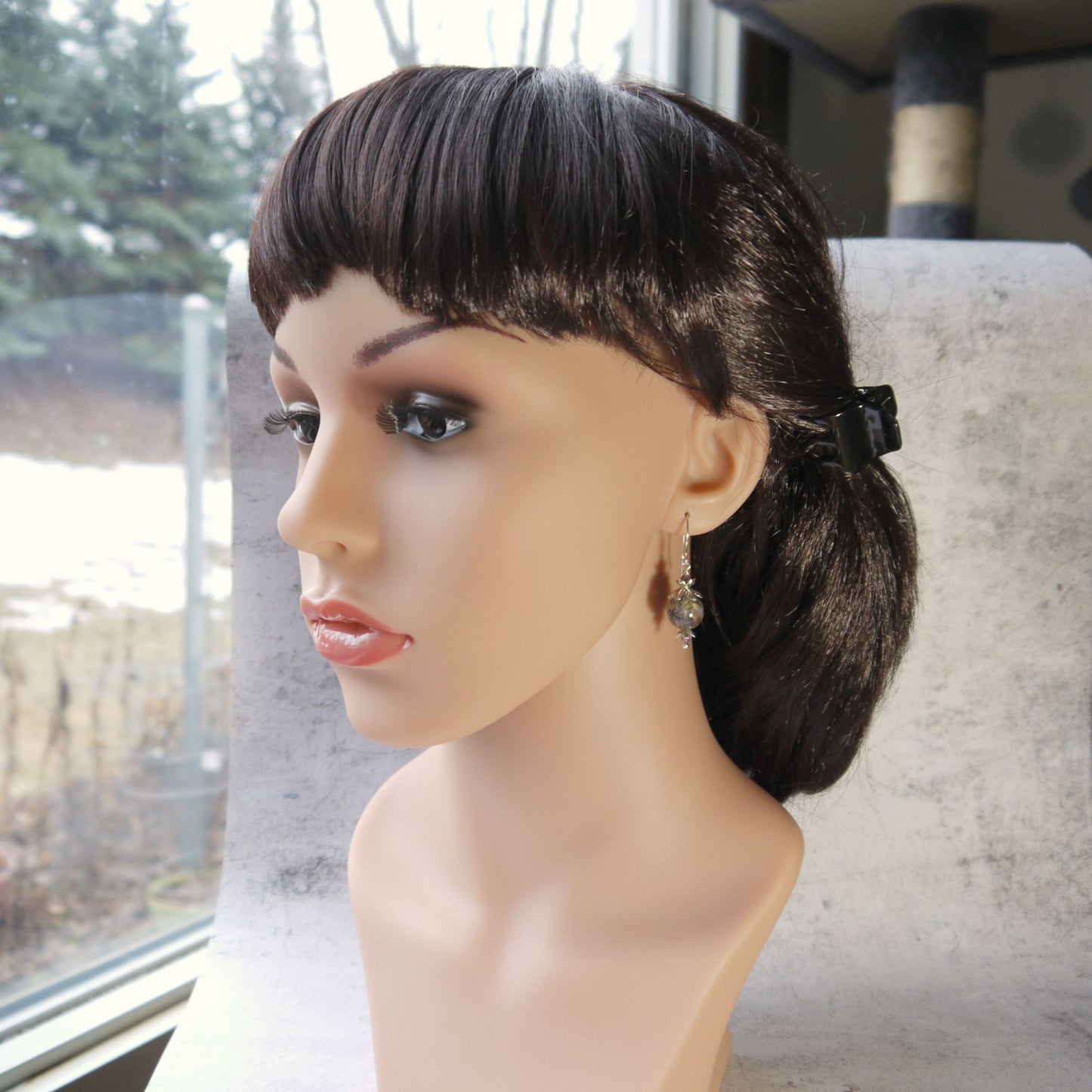 Mannequin head with a styled wig wearing real flower drop earrings on a blurred outdoor background